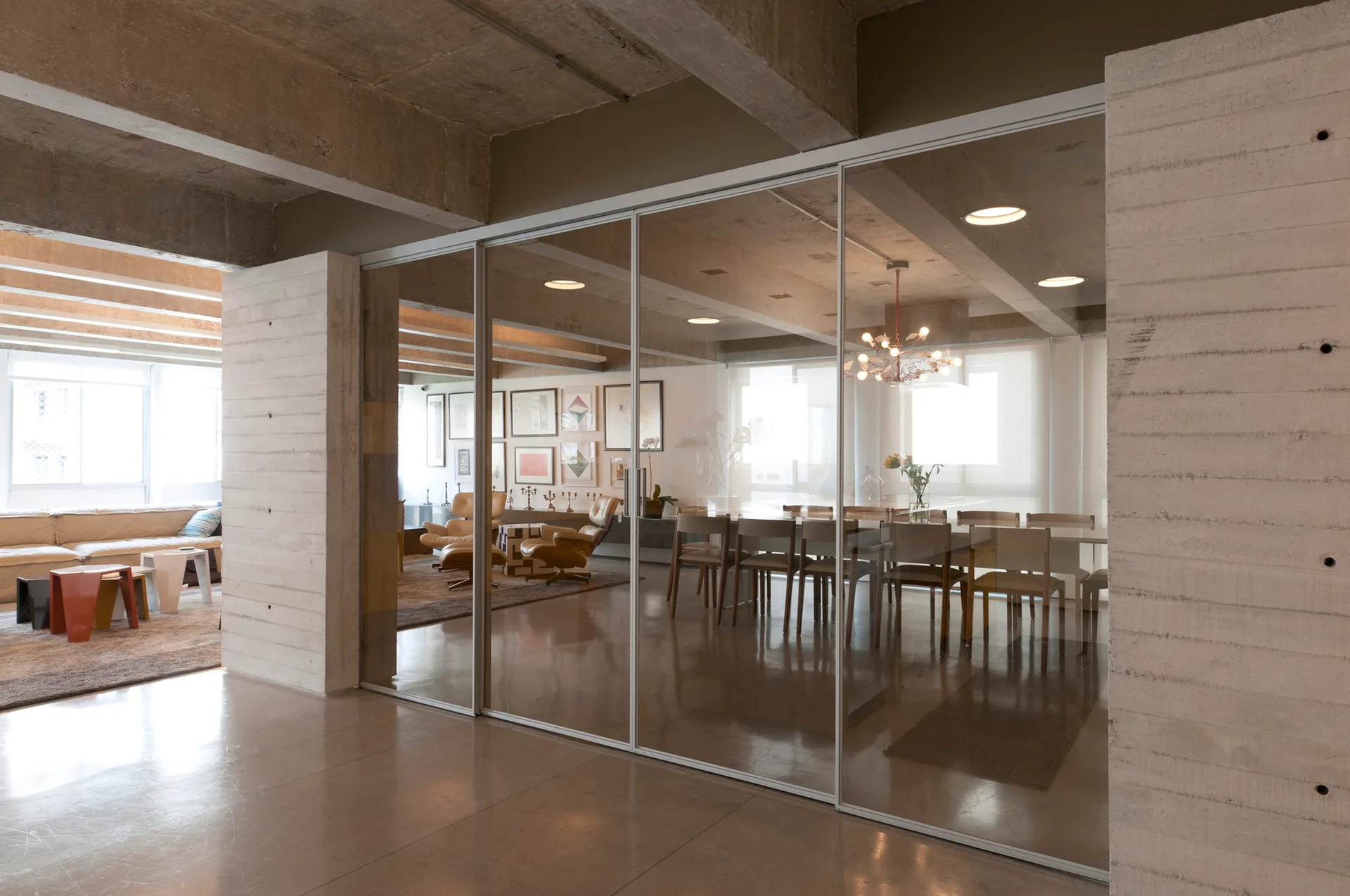An open interior with board-formed concrete walls and a large sliding glass partition dividing the living and dining areas.