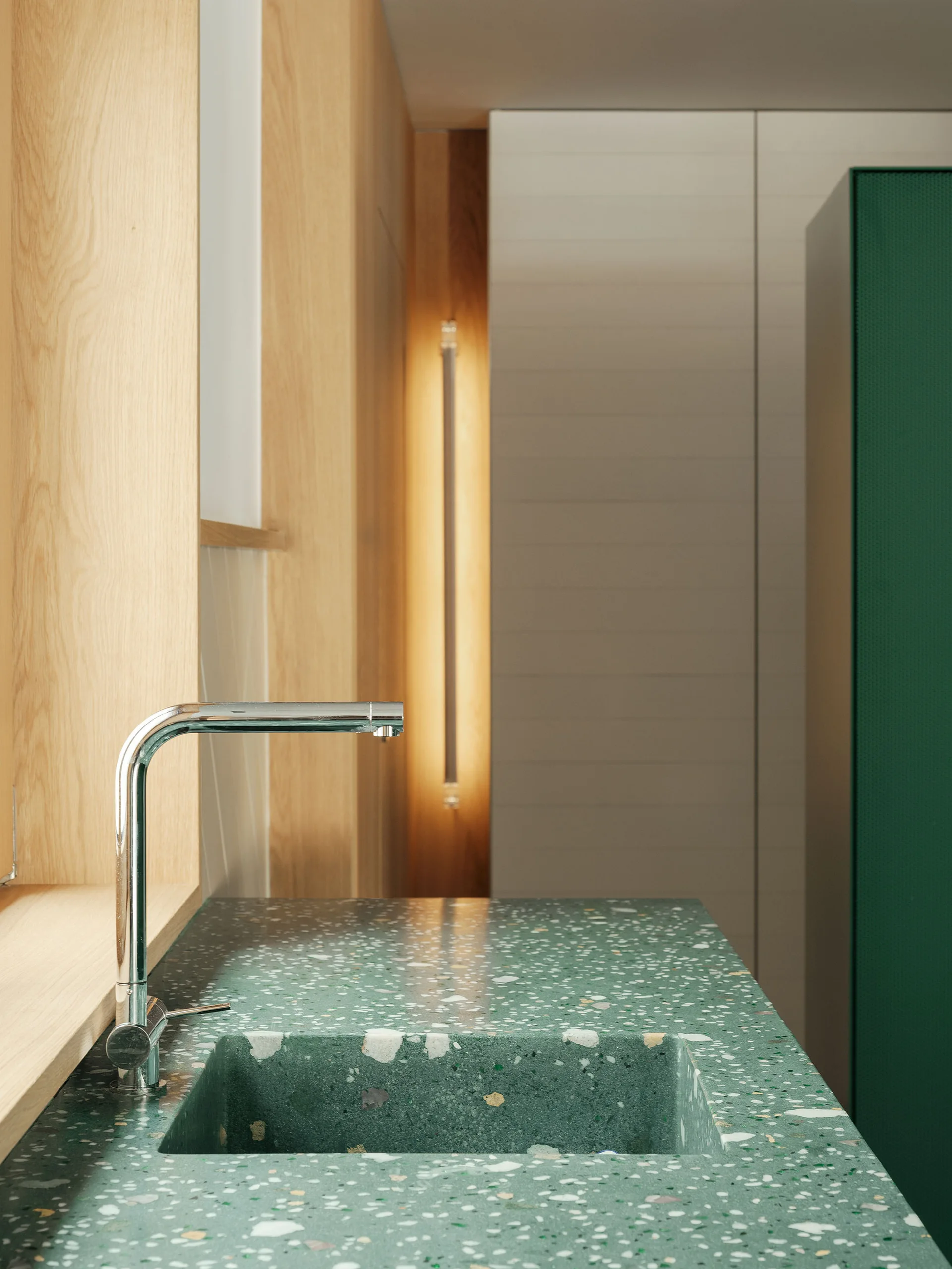 A close-up of a modern bathroom featuring a green terrazzo integrated sink with a chrome faucet, set against warm vertical wood paneling.