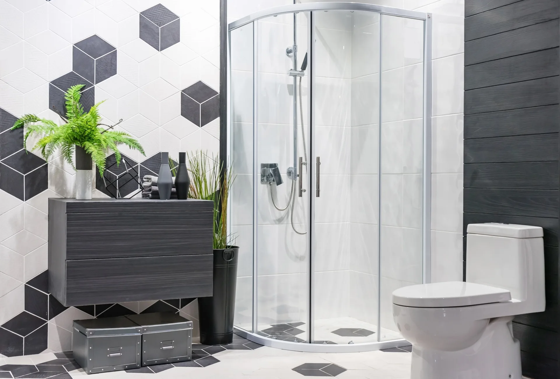 A modern bathroom features a curved glass shower stall, a floating charcoal vanity, and black and white geometric hexagonal wall tile.