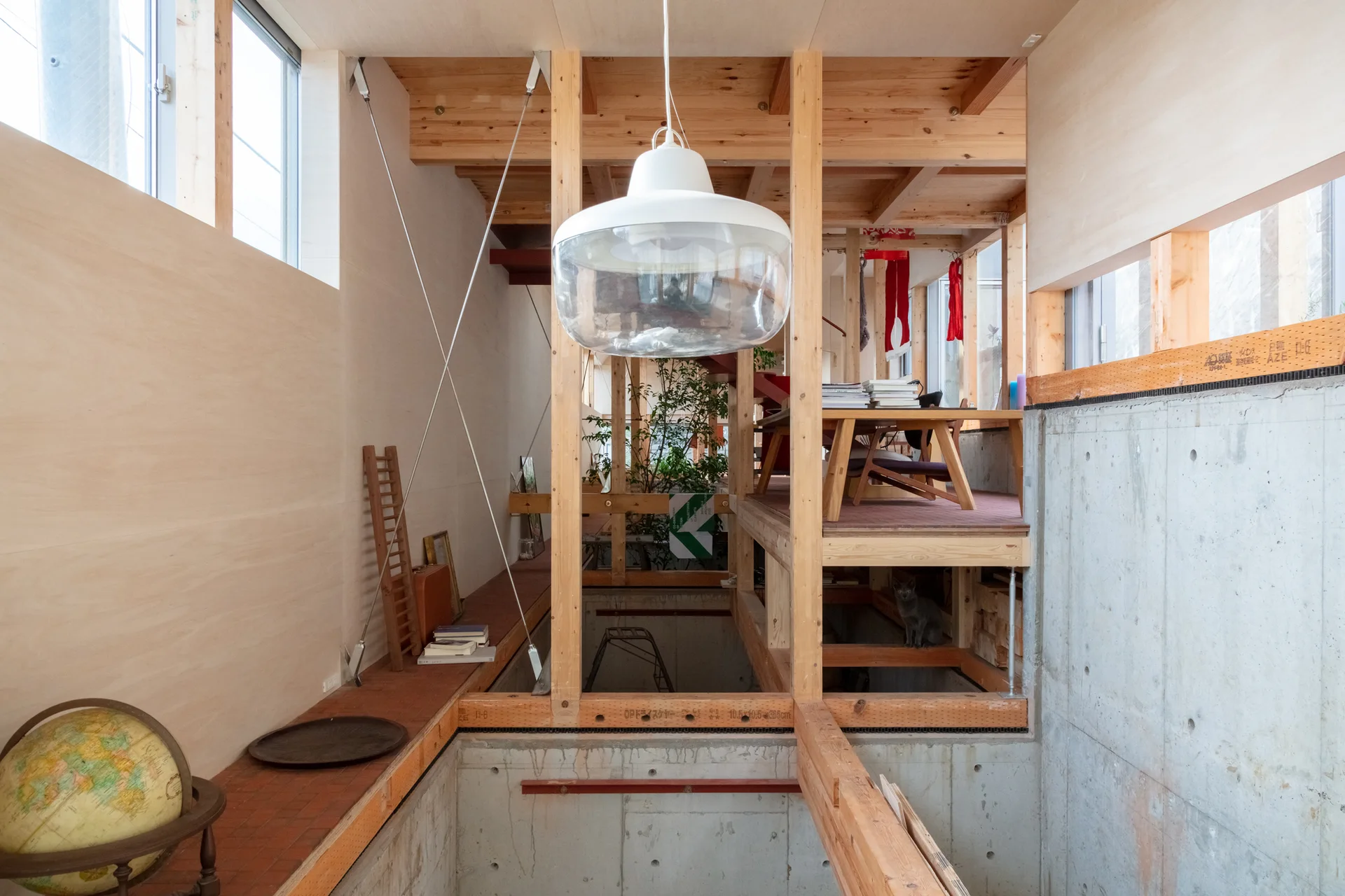 A multi-level home interior featuring exposed timber framing, a raw concrete lower wall, a large white pendant light, and clerestory windows.