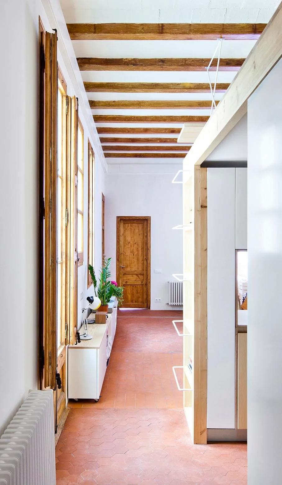 A long hallway features hexagonal terracotta floor tiles, exposed wooden ceiling beams, and tall windows with interior shutters.