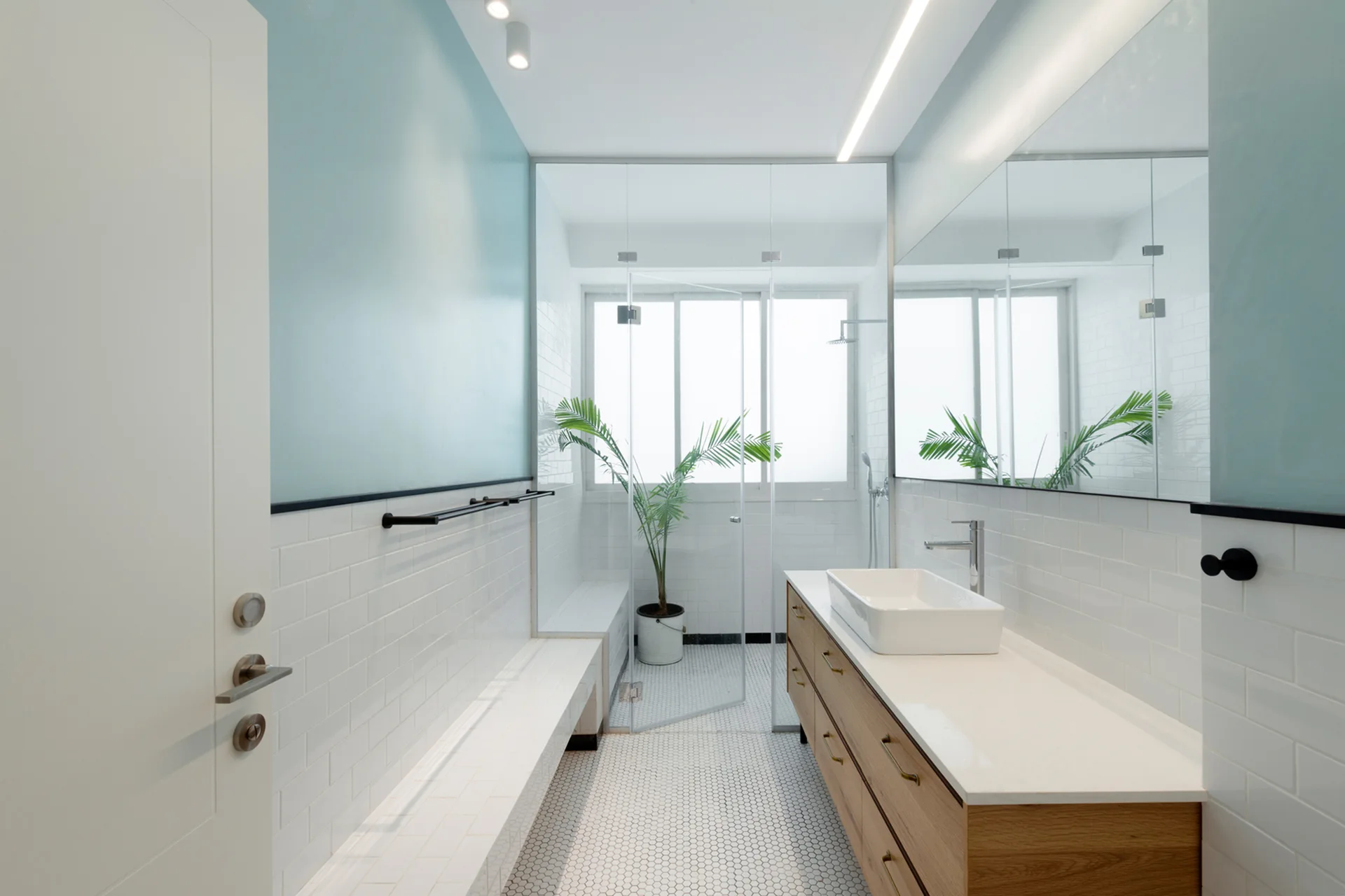 A modern bathroom featuring a floating wood vanity with a white vessel sink, subway wall tiles, and a glass-enclosed shower.