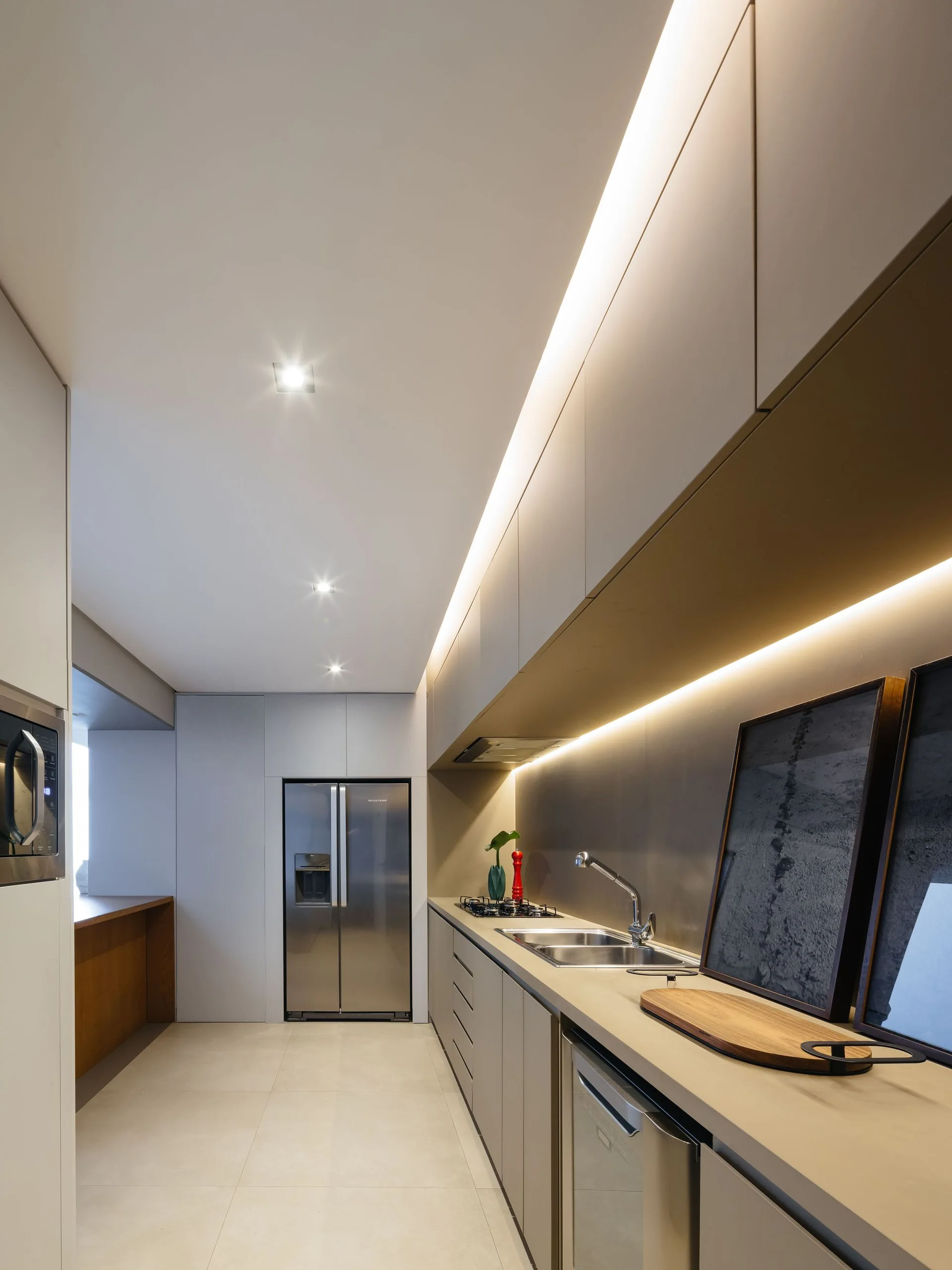A modern galley kitchen features matte beige cabinets, stainless steel appliances, and glowing strip lights under and above the overhead cabinetry.