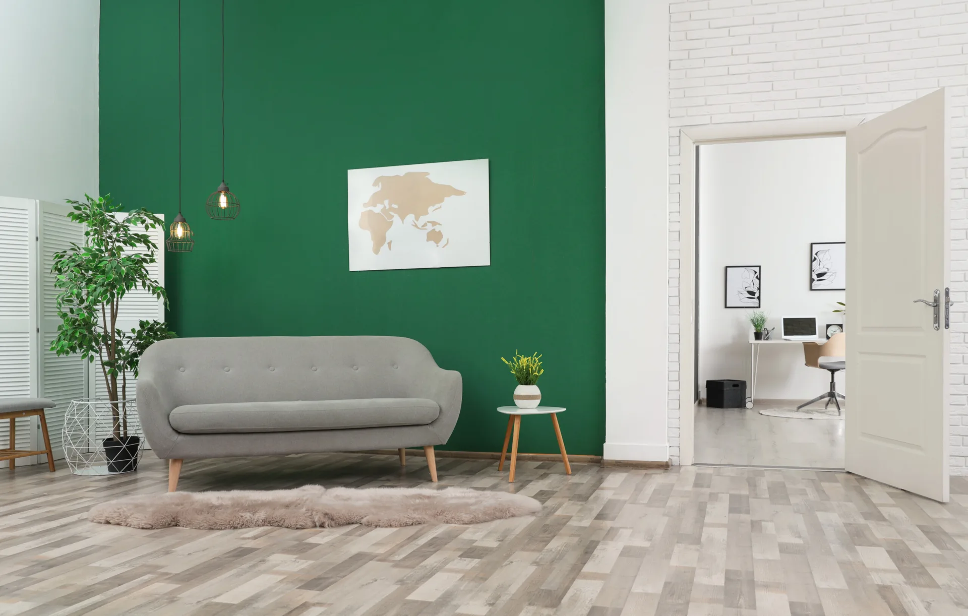 A grey mid-century modern sofa sits against a vibrant green accent wall next to an open doorway showing a home office.