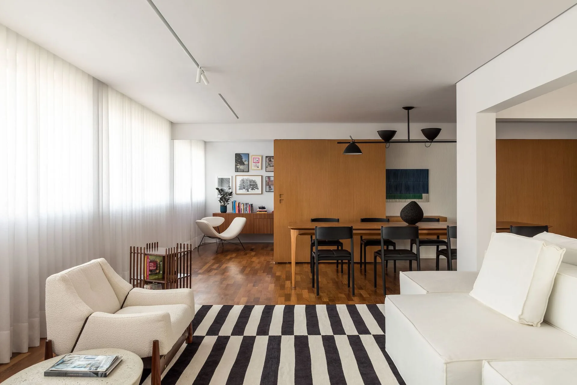 A modern open-concept living and dining area features a black and white striped rug, a wooden dining set, and a large sliding wood door.