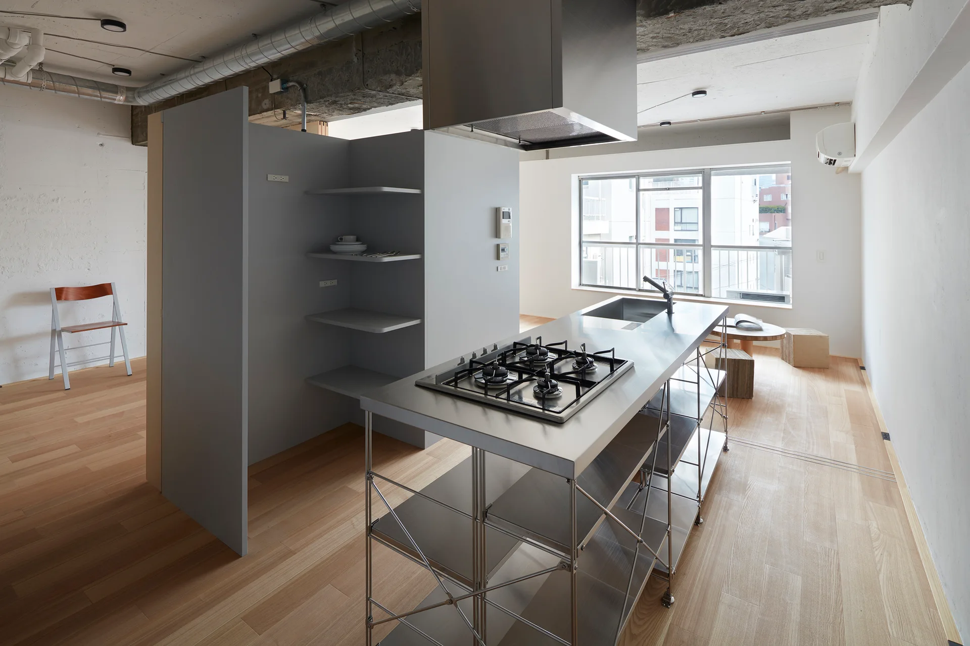 An open-plan loft kitchen features a stainless steel island, a gray partition wall with built-in shelves, and exposed ceiling ducts.