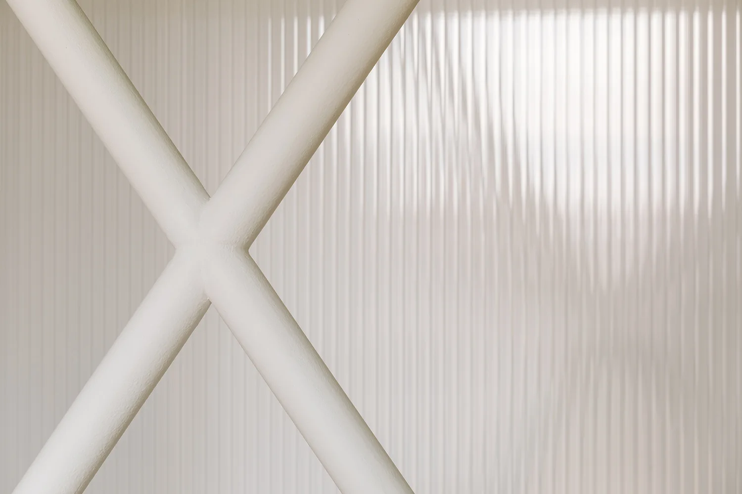 A close-up shot of a white matte tubular metal X-brace positioned against a translucent fluted glass panel with vertical ridges.