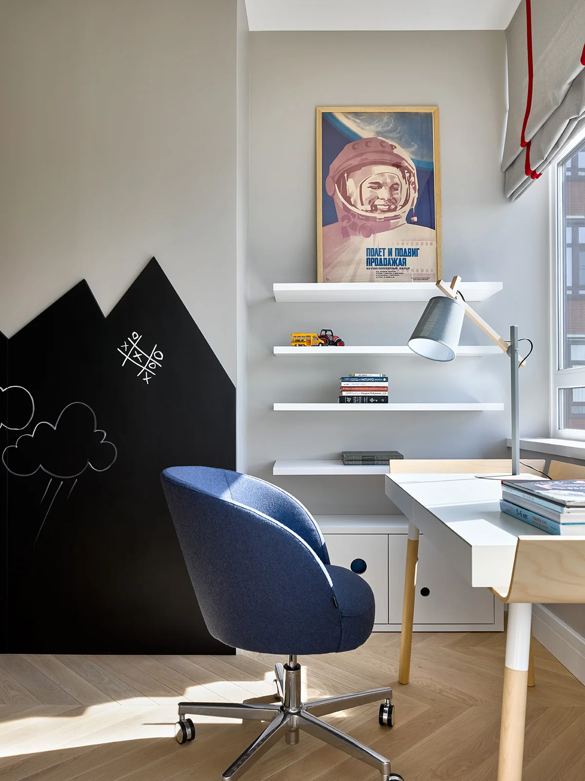 A modern childrens study area features a white desk, blue upholstered swivel chair, and a black mountain-shaped chalkboard wall on herringbone flooring.