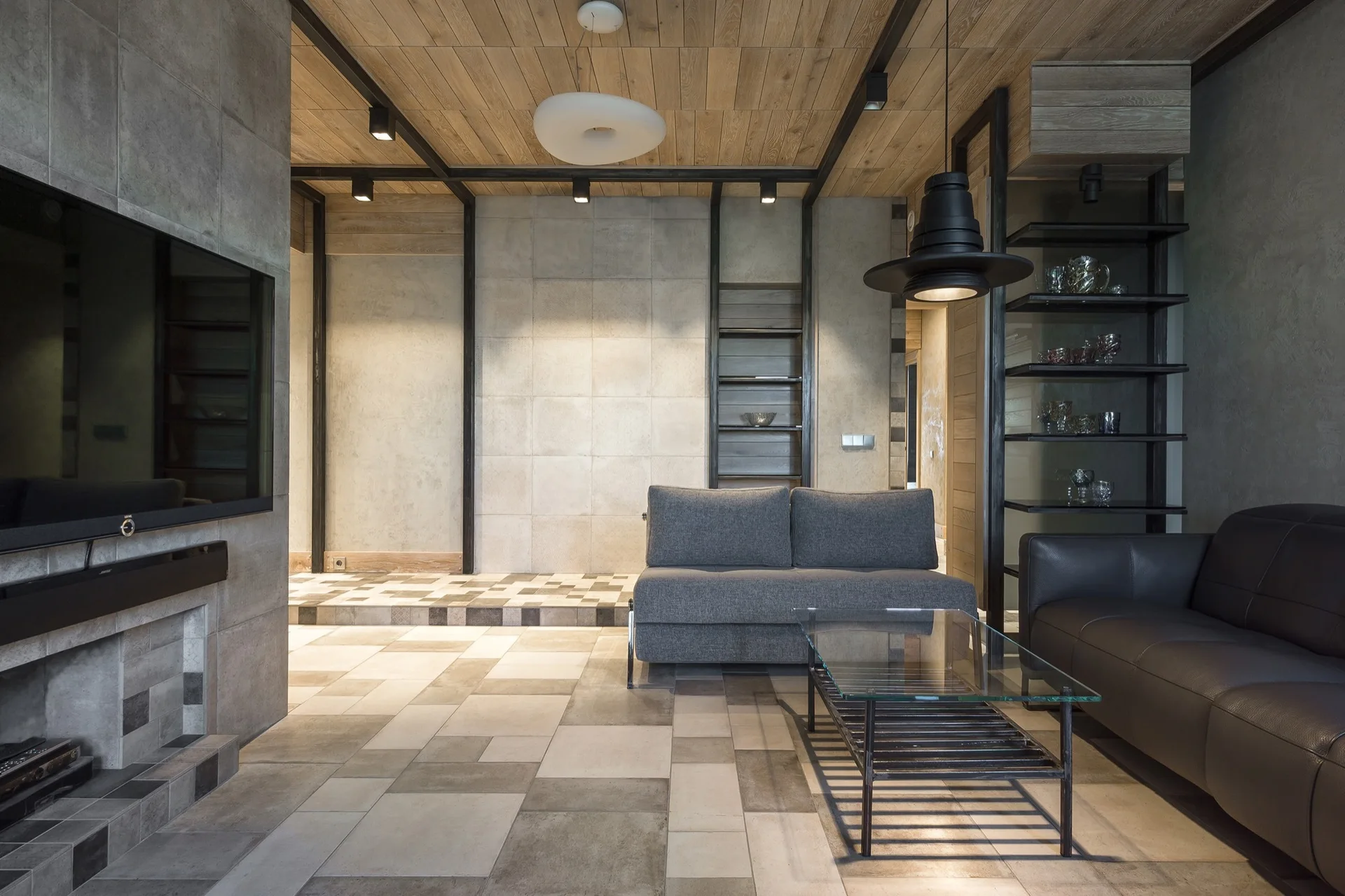 An industrial living room featuring a wood plank ceiling with metal beams, concrete-like tile walls, and a gray sofa near a glass coffee table.