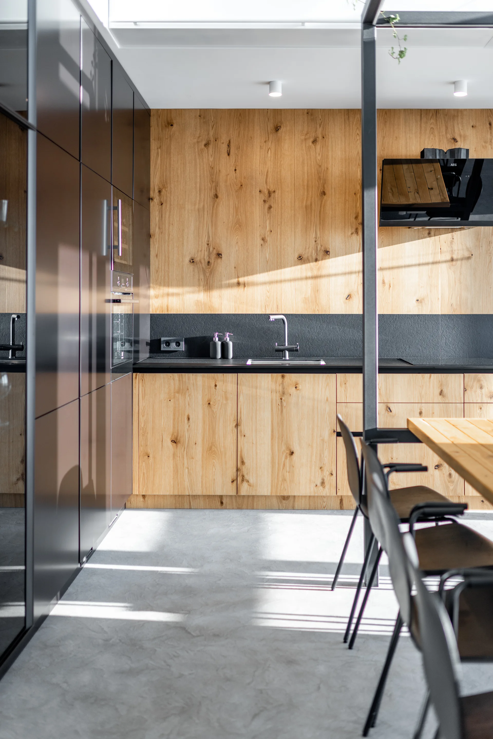 A minimalist kitchen features sleek flat-front wood cabinets, high-gloss dark tall cabinetry, a concrete floor, and a matching wood dining table.