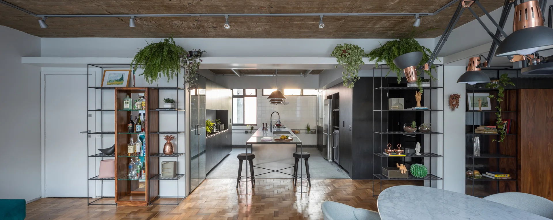 An industrial open-plan kitchen featuring a raw concrete ceiling, herringbone parquet wood floors, and black metal frame shelving.