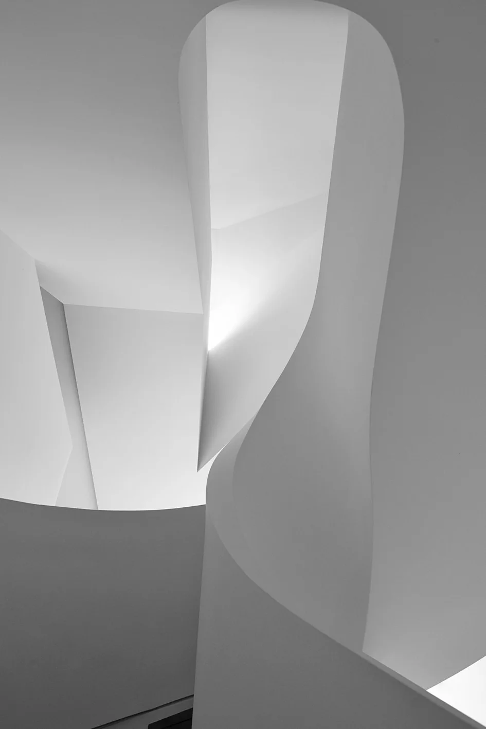 A close-up view of a minimalist white staircase featuring sculptural curved walls, sharp geometric angles, and matte plaster-like surfaces.