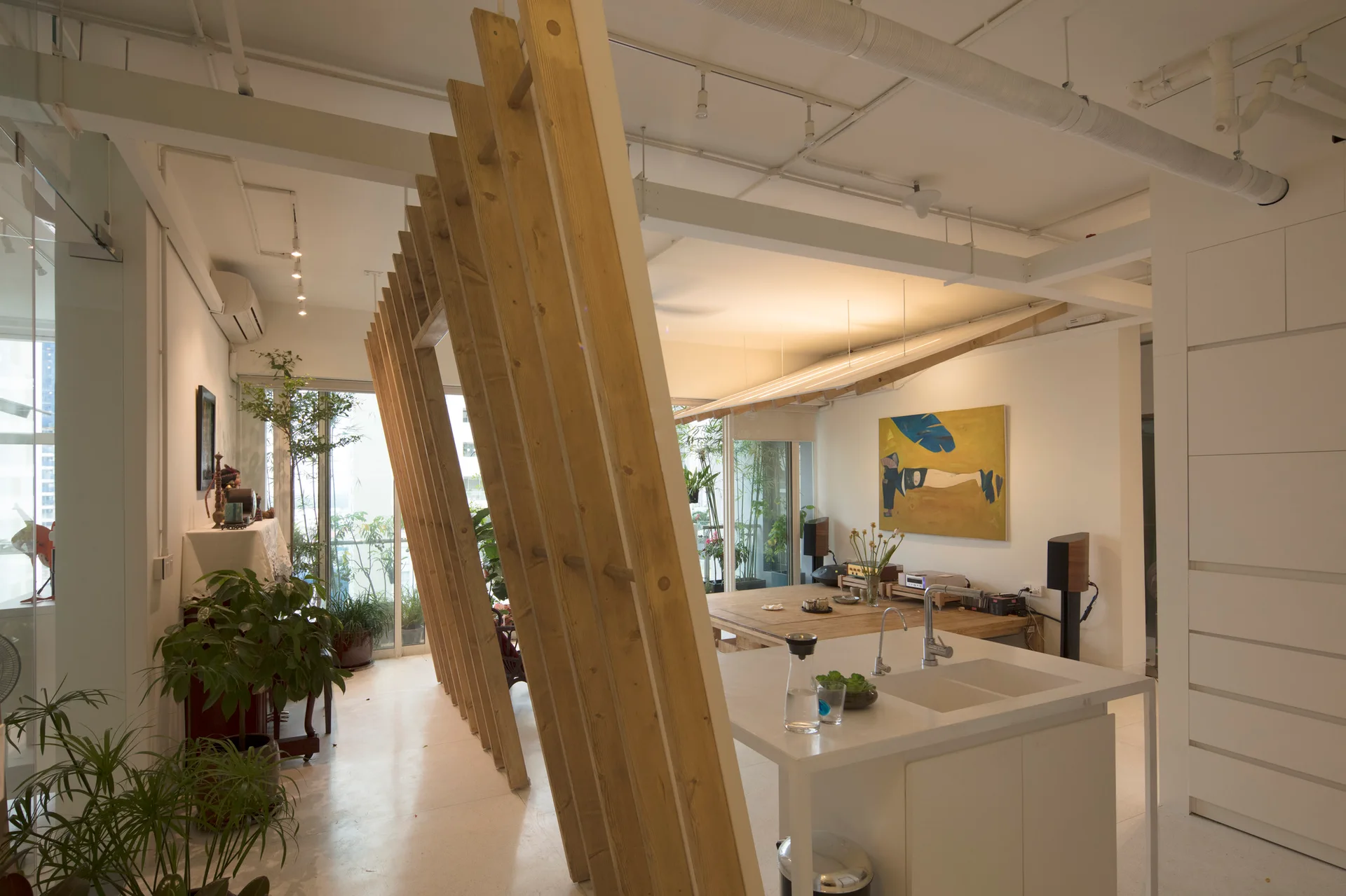 A modern open-plan interior featuring a white kitchen island in the foreground and a slanted wooden slat partition screen.