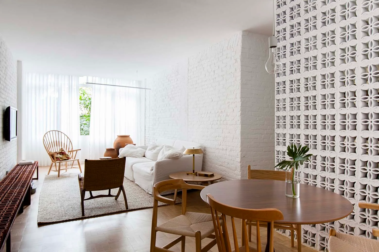 A bright living room features a white painted brick wall, a slipcovered sofa, herringbone parquet flooring, and a white breeze block partition.