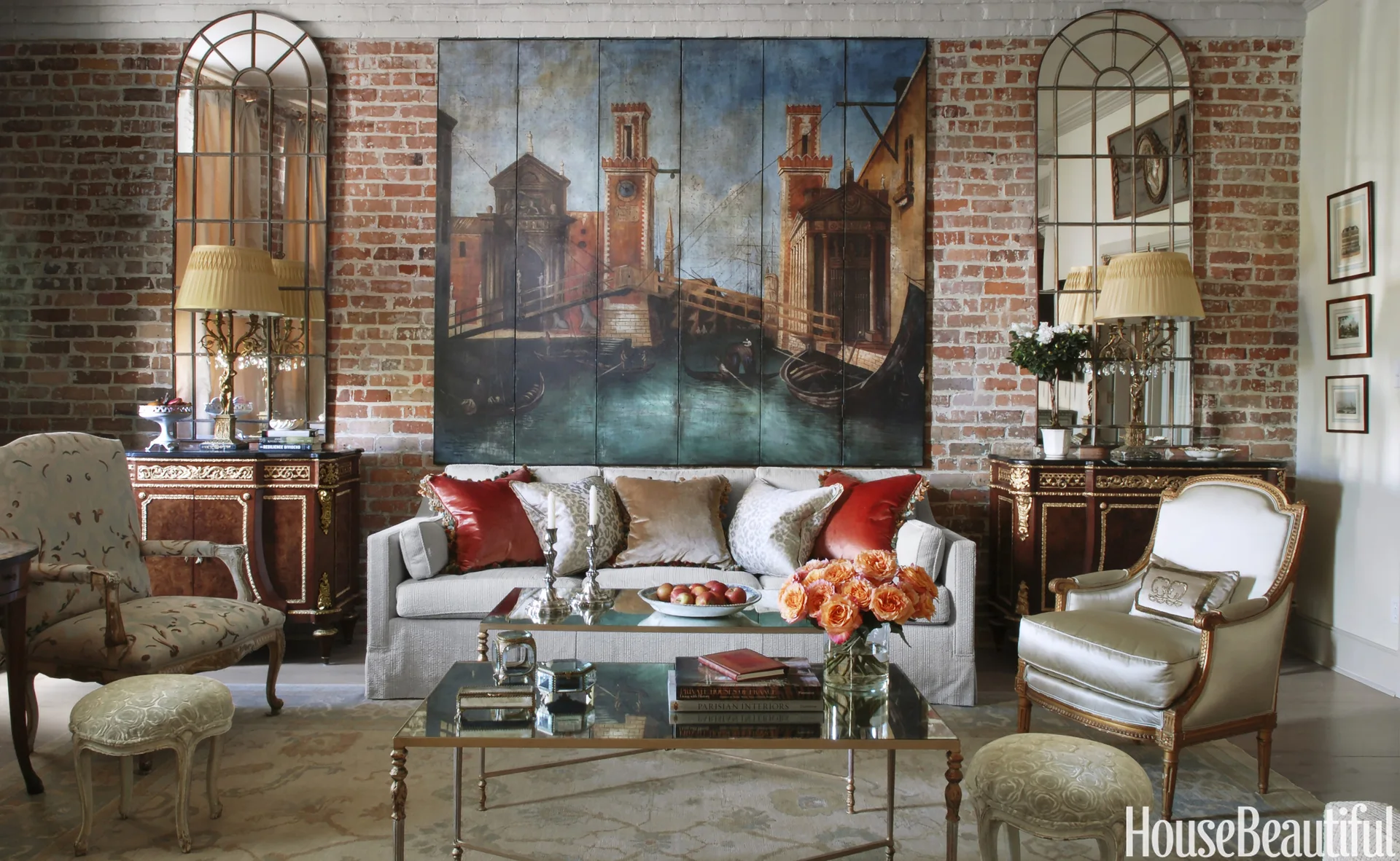 A formal living room featuring a cream sofa in front of an exposed brick wall decorated with a large painting and two arched mirrors.