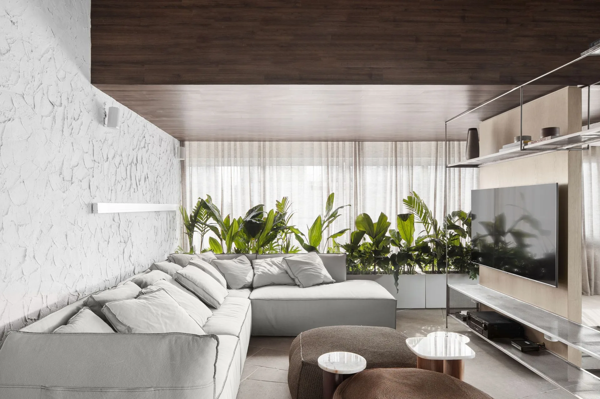 A minimalist living room showing a light grey sectional sofa set against a textured white plaster wall beneath a dark wood ceiling.
