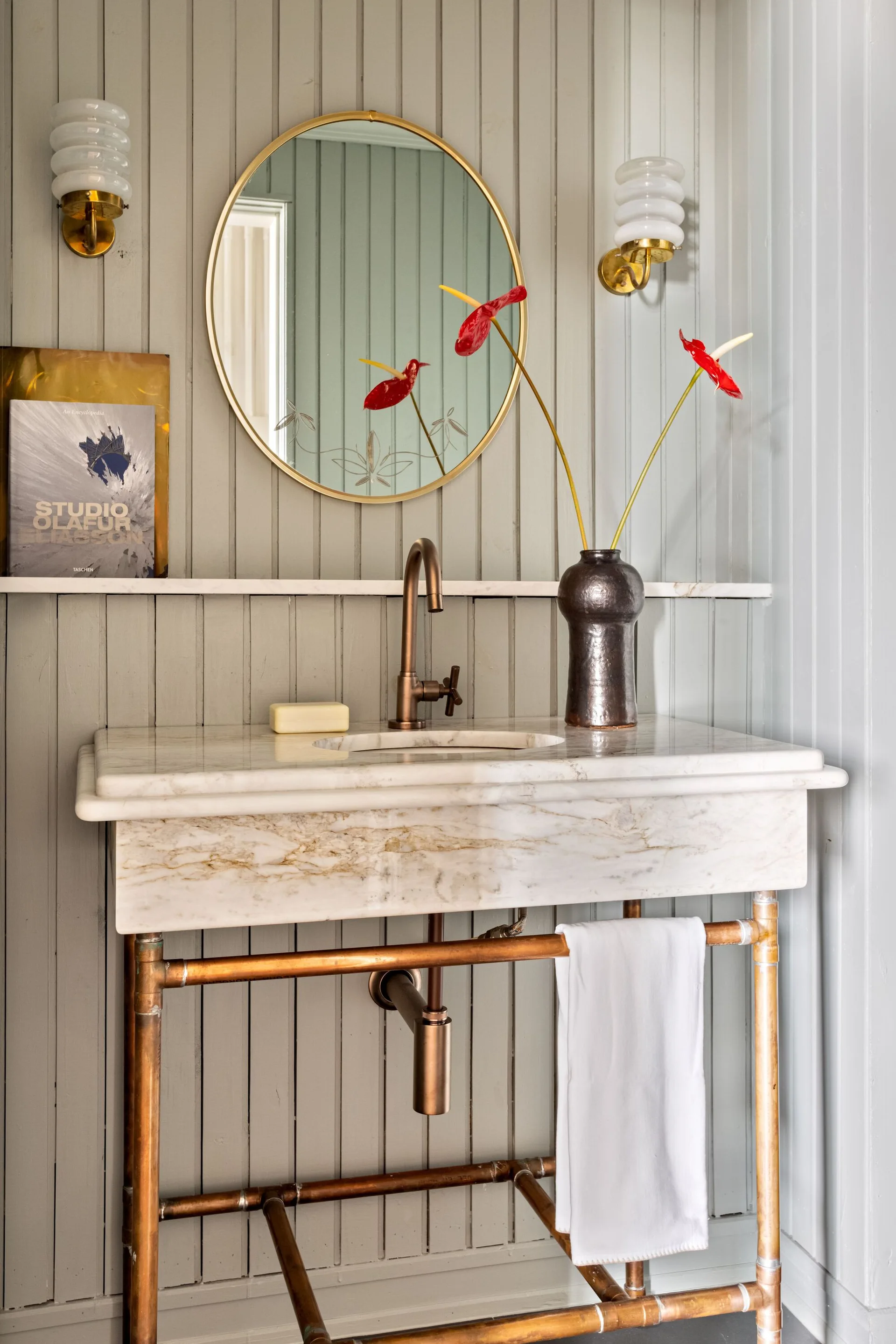 A bathroom vanity featuring a thick marble top on a copper pipe stand against light grey beadboard wall paneling.