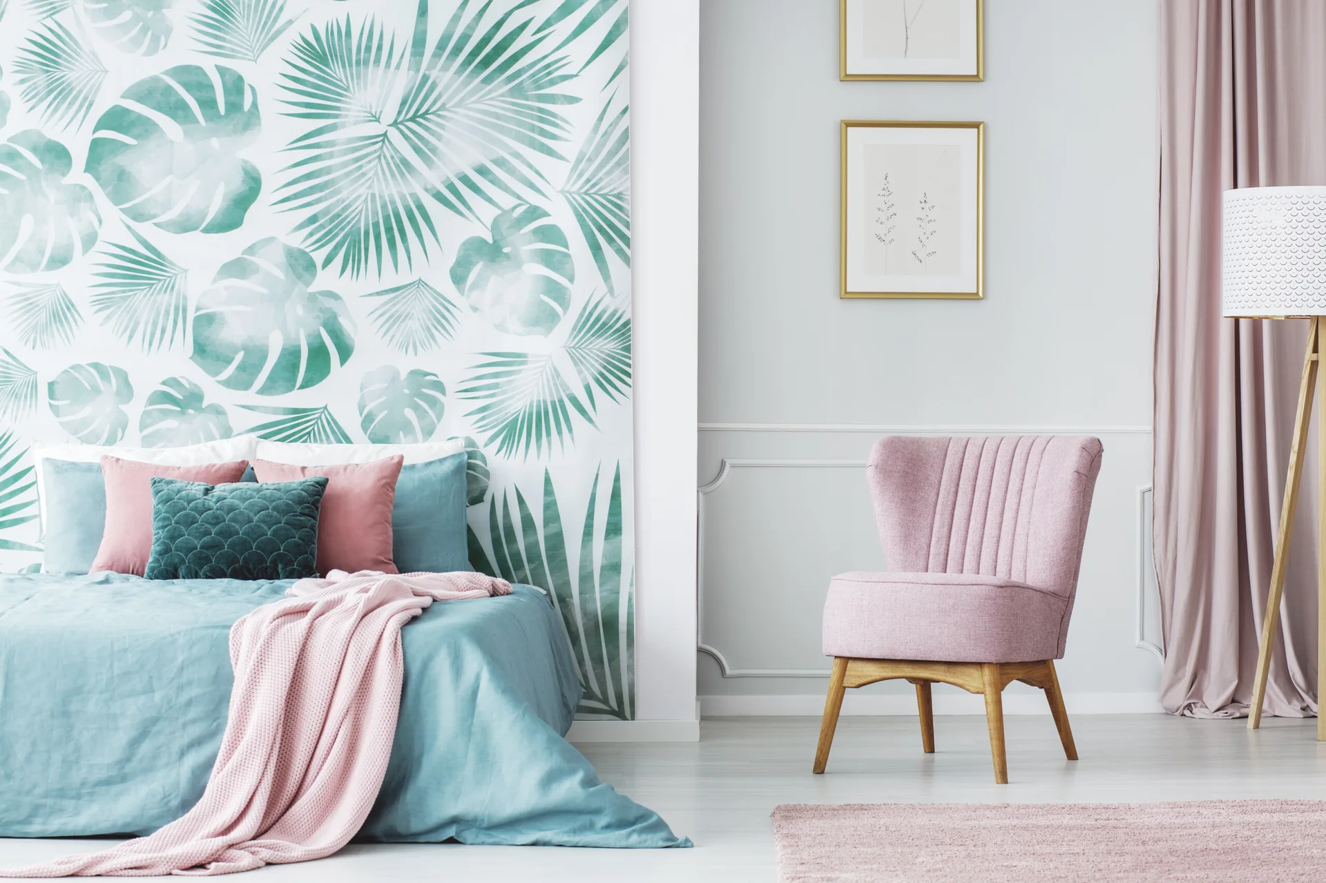 A contemporary bedroom featuring a green botanical wallpaper accent wall behind a teal bed, next to a pink upholstered chair.
