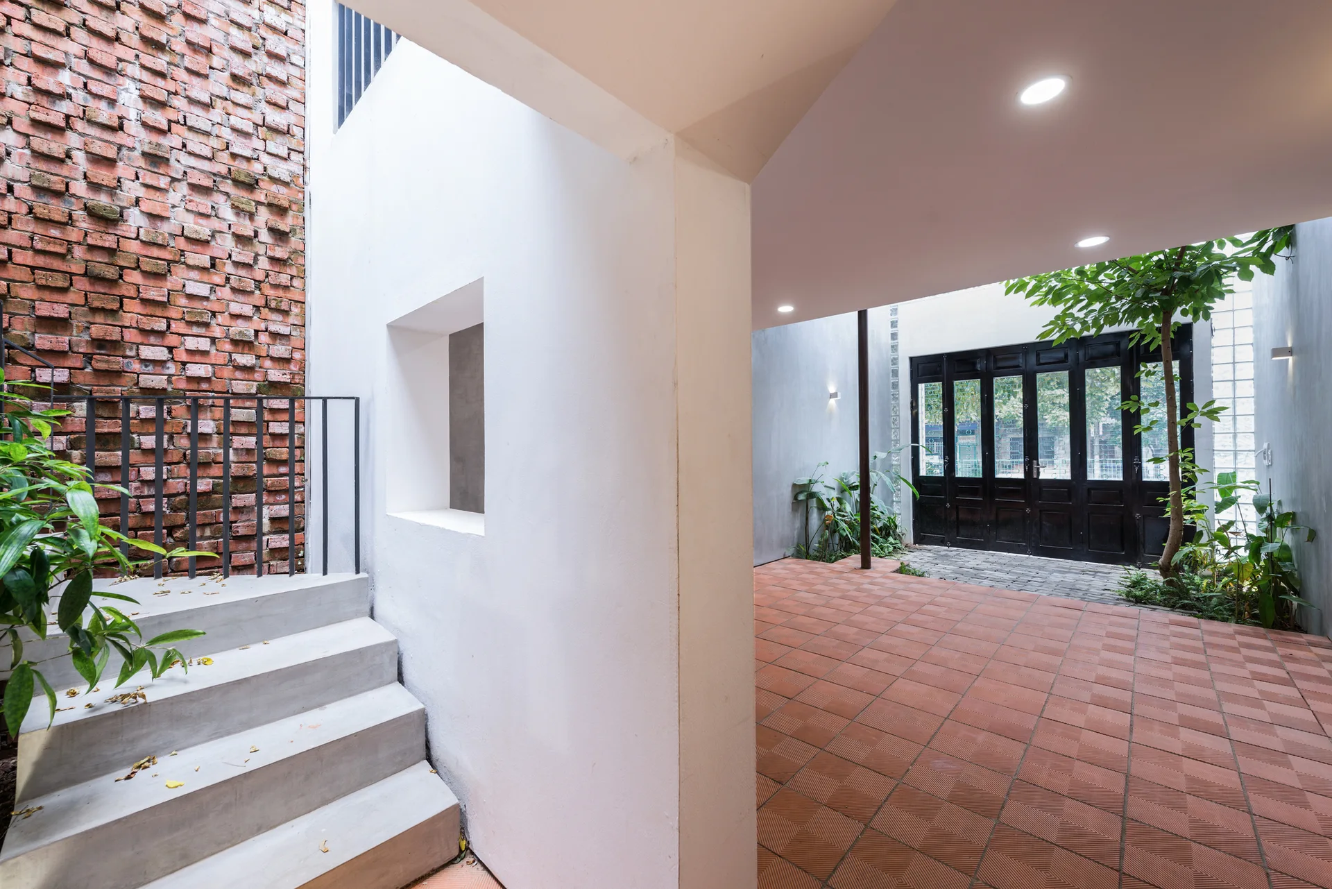 A modern courtyard entryway features concrete steps alongside a textured brick wall, white plaster walls, and patterned terracotta floor tiles.