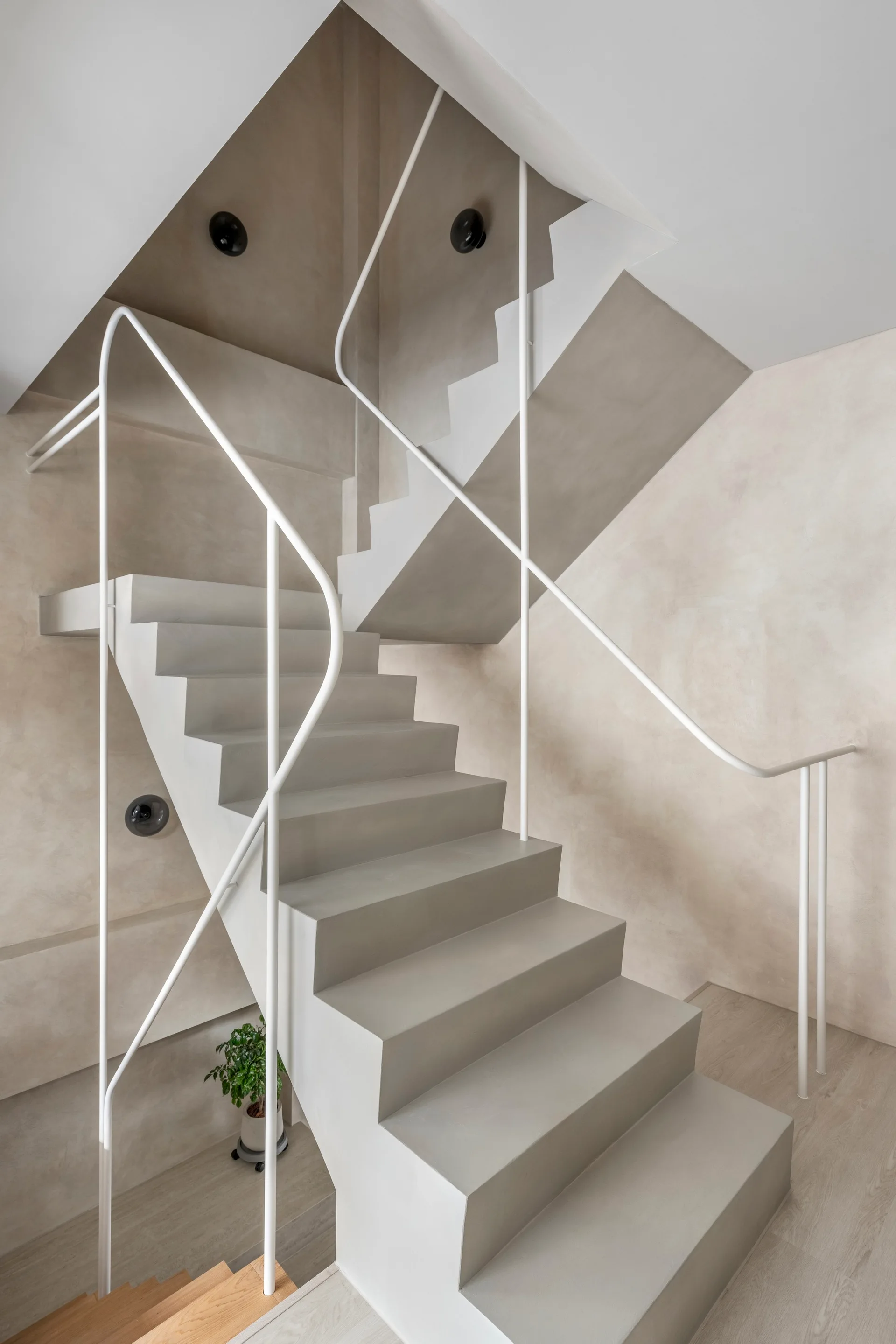 A minimalist light gray concrete staircase with a thin white metal railing stands against a textured beige plaster wall.