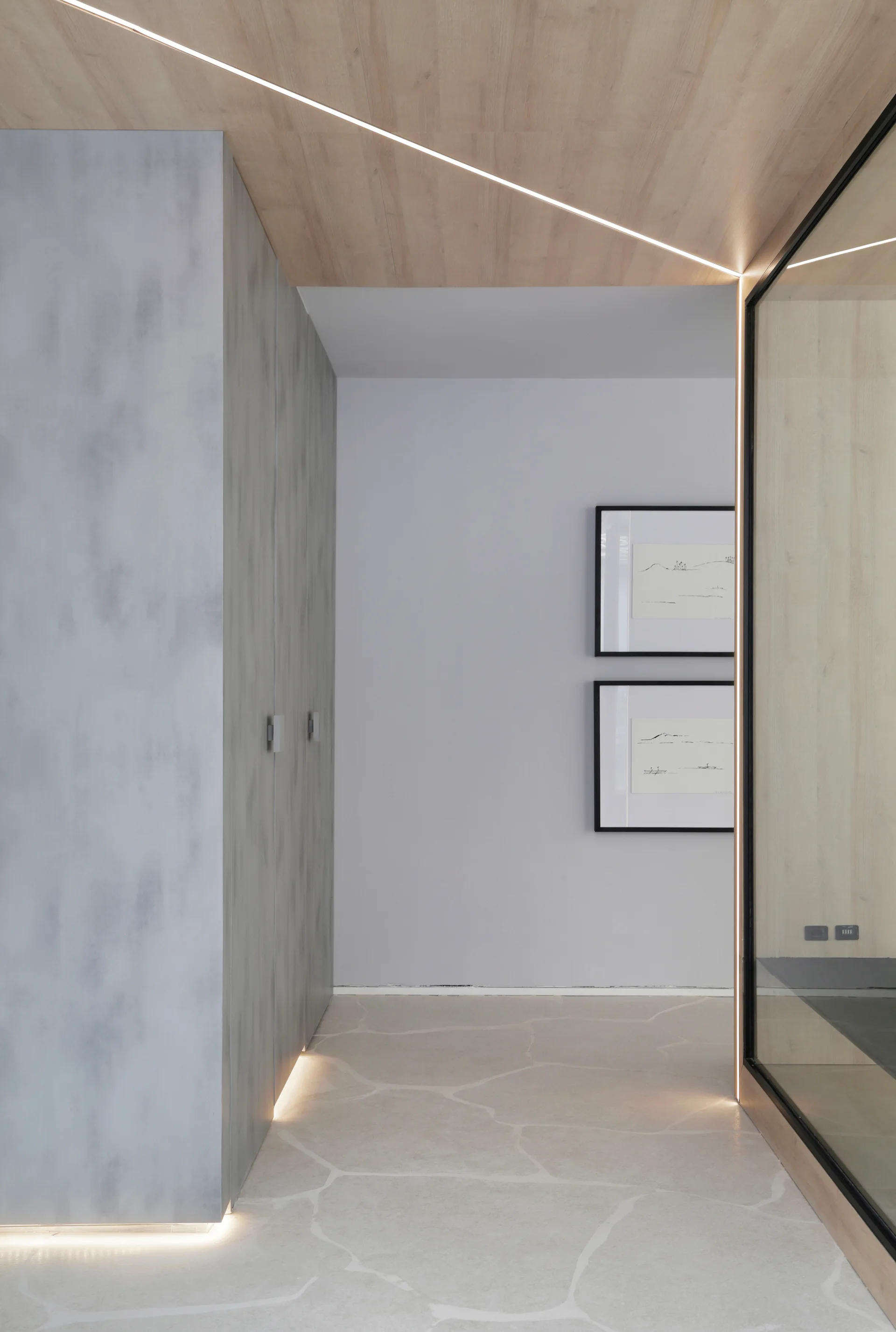 A contemporary hallway features a wood-paneled ceiling with a recessed linear light, grey built-in cabinets, and a veined stone floor.