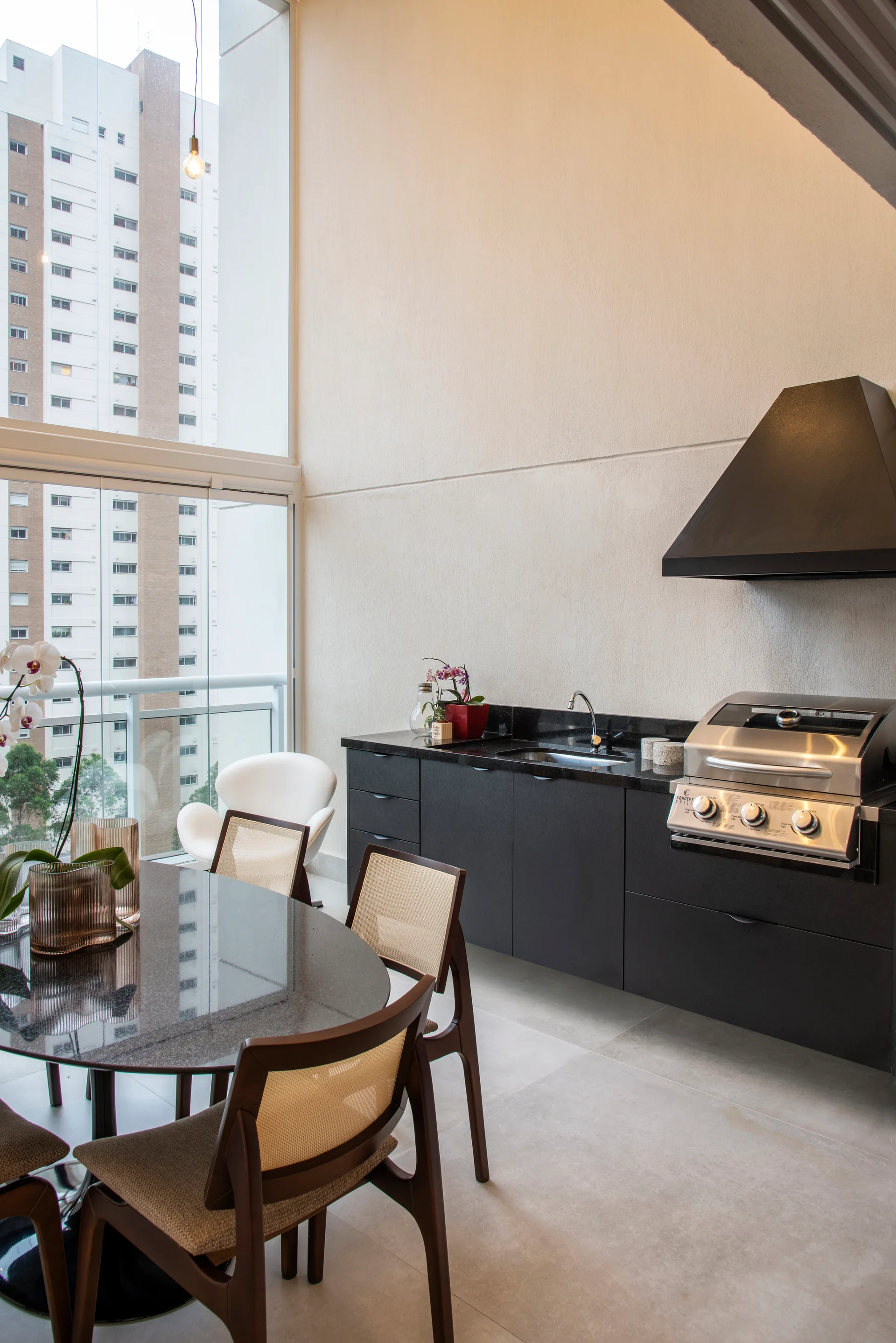 A high-rise balcony kitchen features matte black cabinetry, an integrated grill, and a round dark dining table with cane-back chairs.