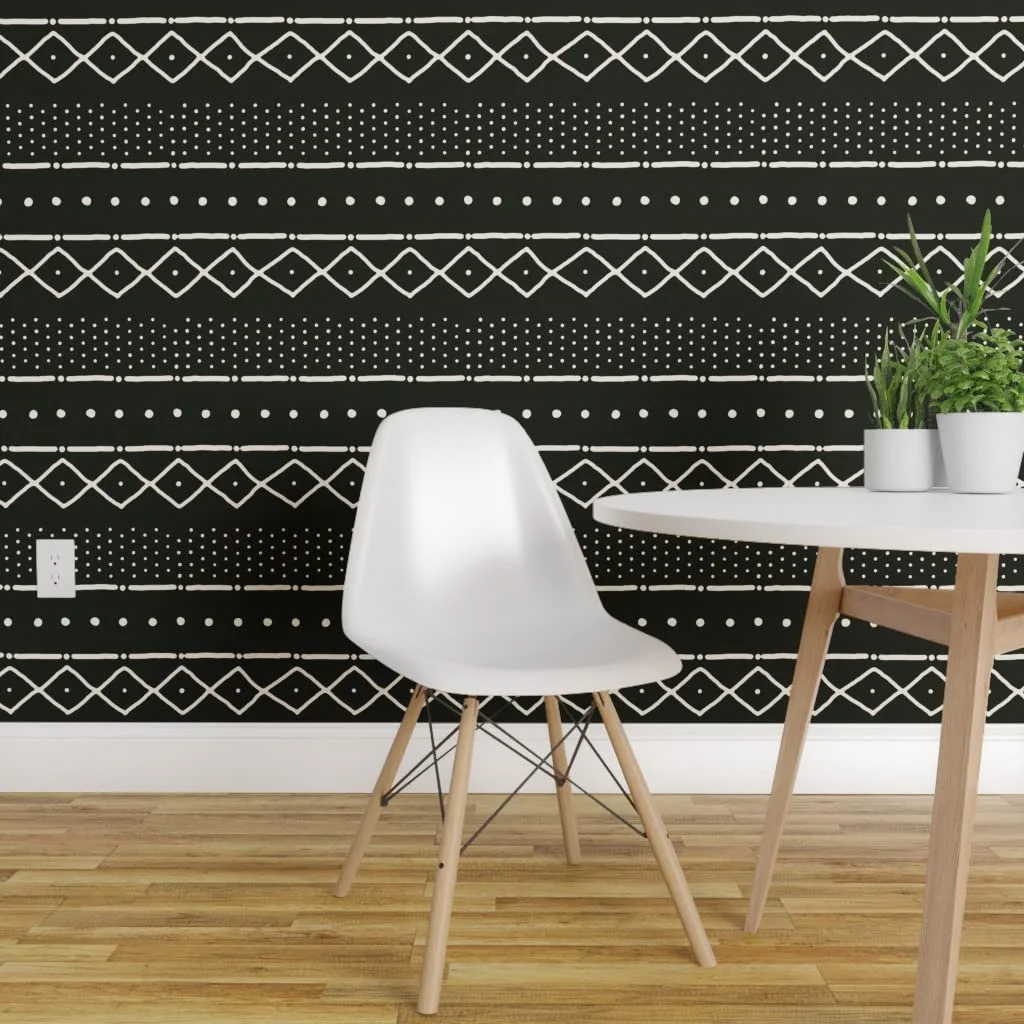 A white molded plastic dining chair and a round table sit in front of a black wall featuring a white hand-drawn geometric pattern.