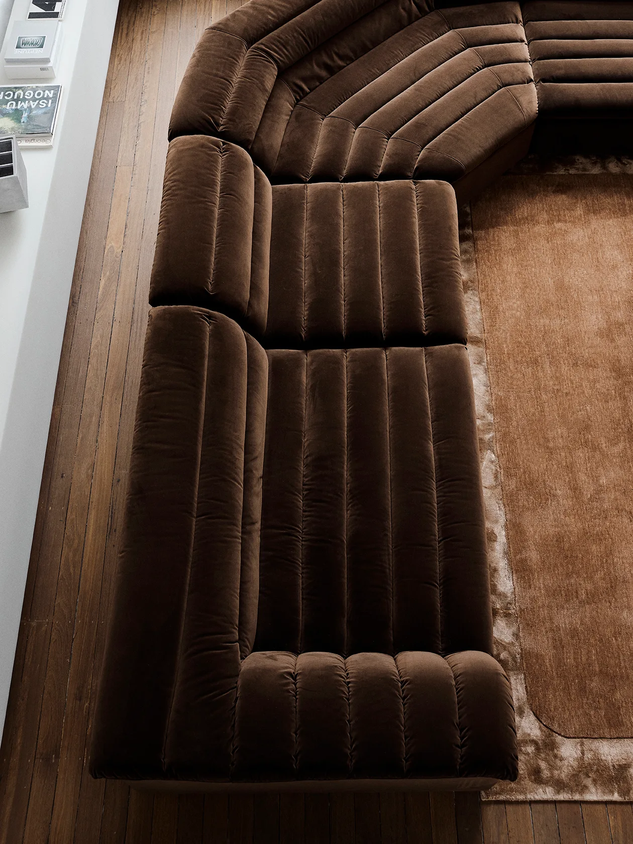 An overhead view of a large brown velvet sectional sofa with channel tufting on hardwood floors next to a matching brown rug.