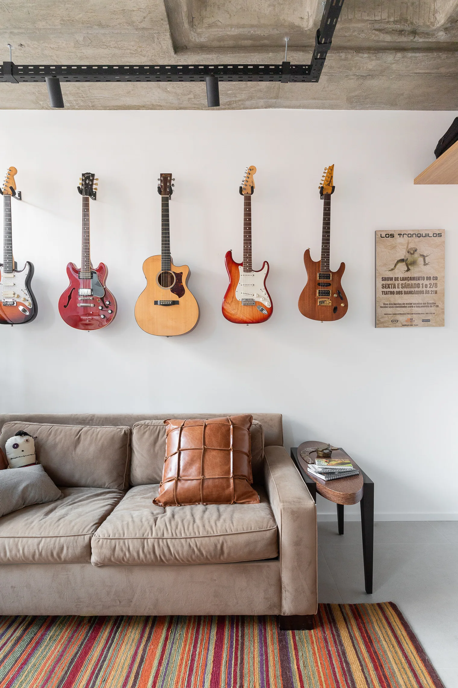 Five electric and acoustic guitars hang in a neat row on a white wall above a tan fabric sofa with a striped rug.