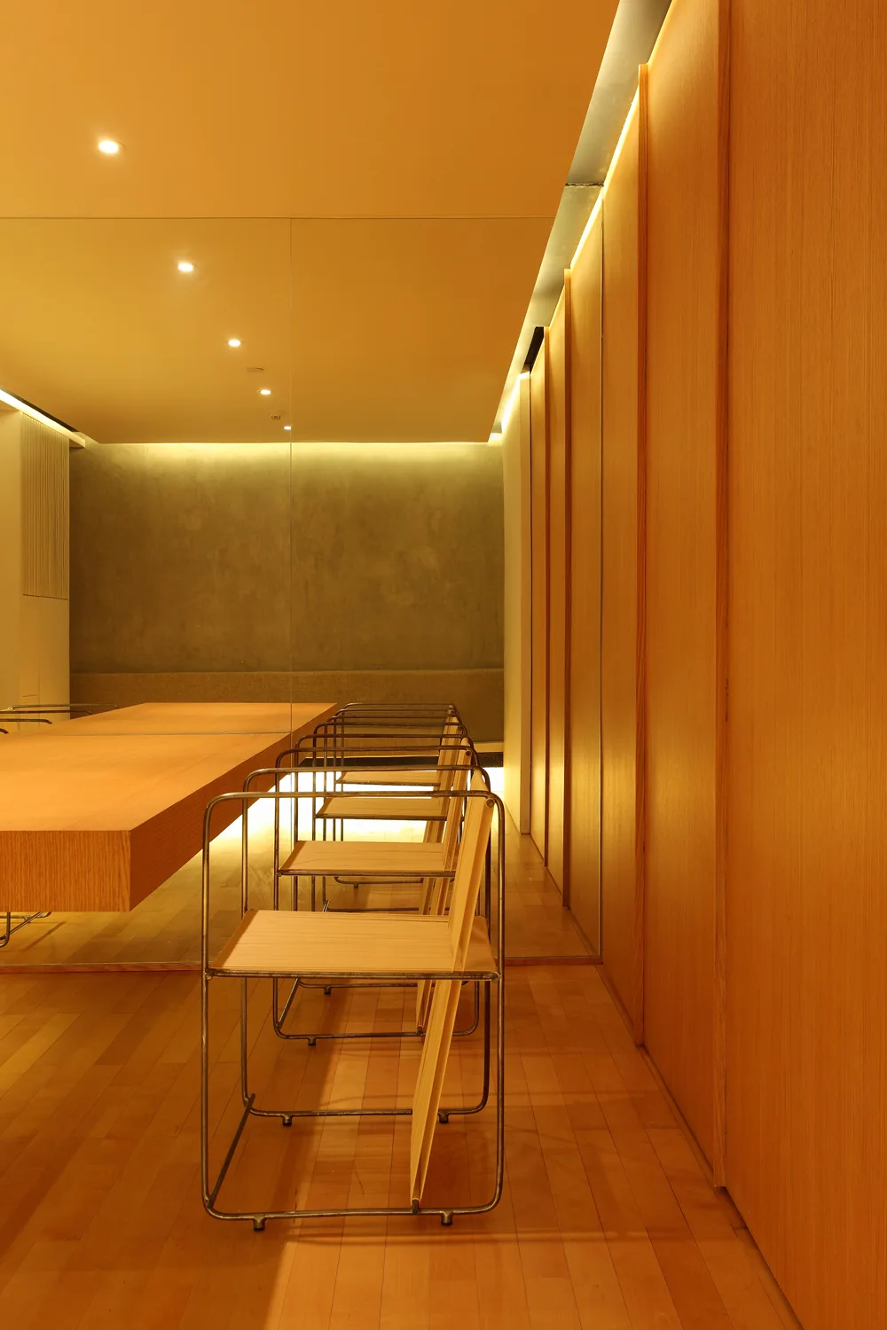 A modern dining area features a long wood table, metal-framed chairs, vertical wood wall paneling, and warm recessed cove lighting.
