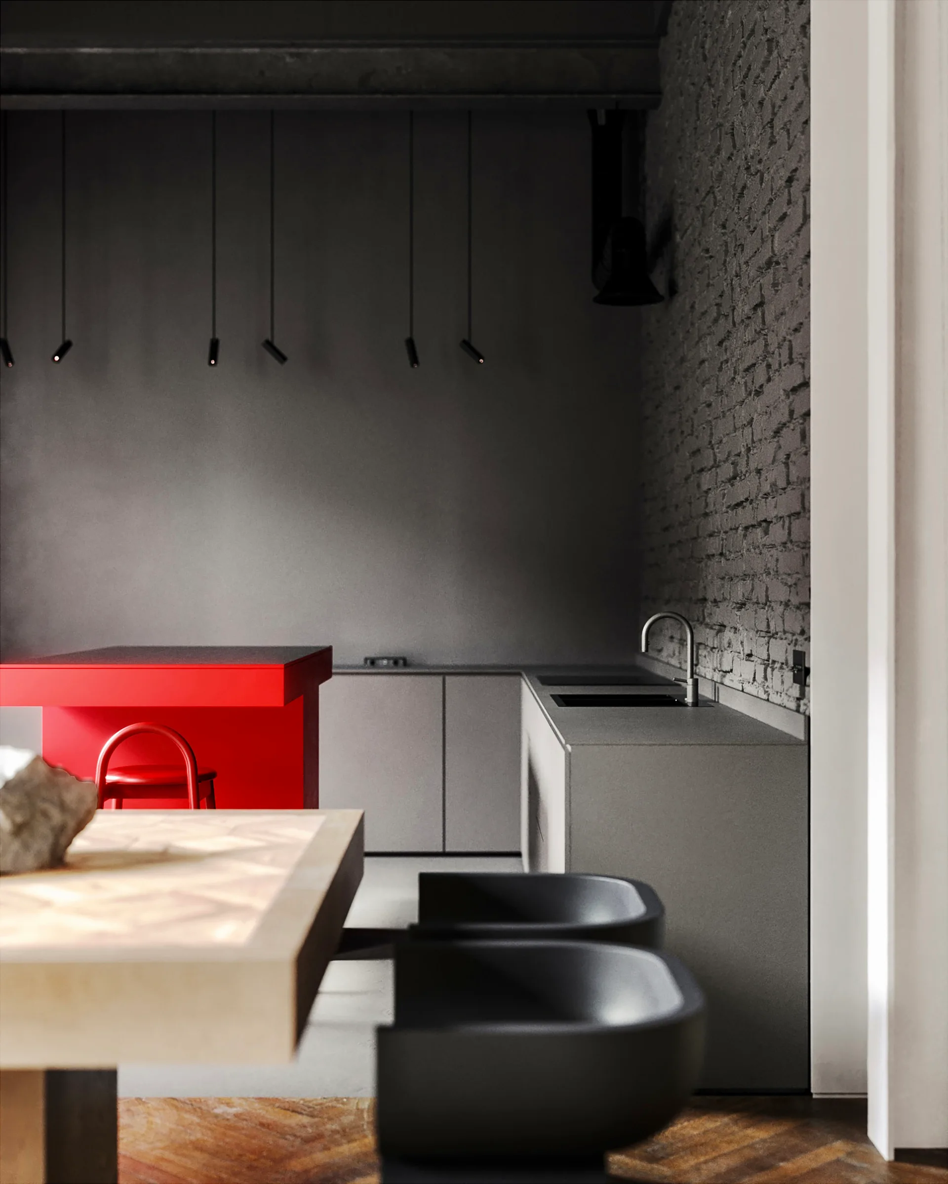 A minimalist dark grey kitchen features a bright red kitchen island, matte grey cabinetry, an exposed brick wall, and sleek black stools.