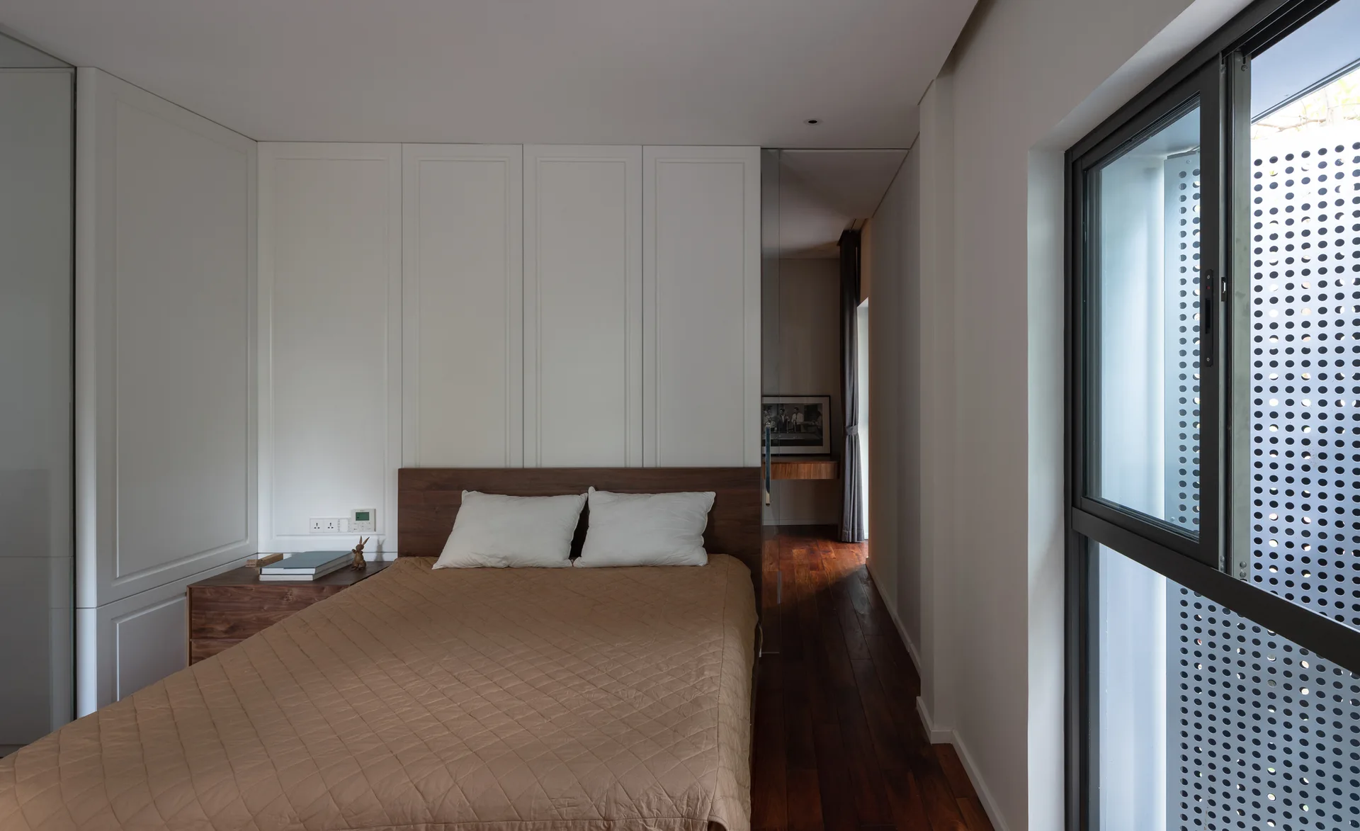 A modern bedroom with a bed featuring a brown quilted cover and a seamless white paneled cabinetry wall behind it.