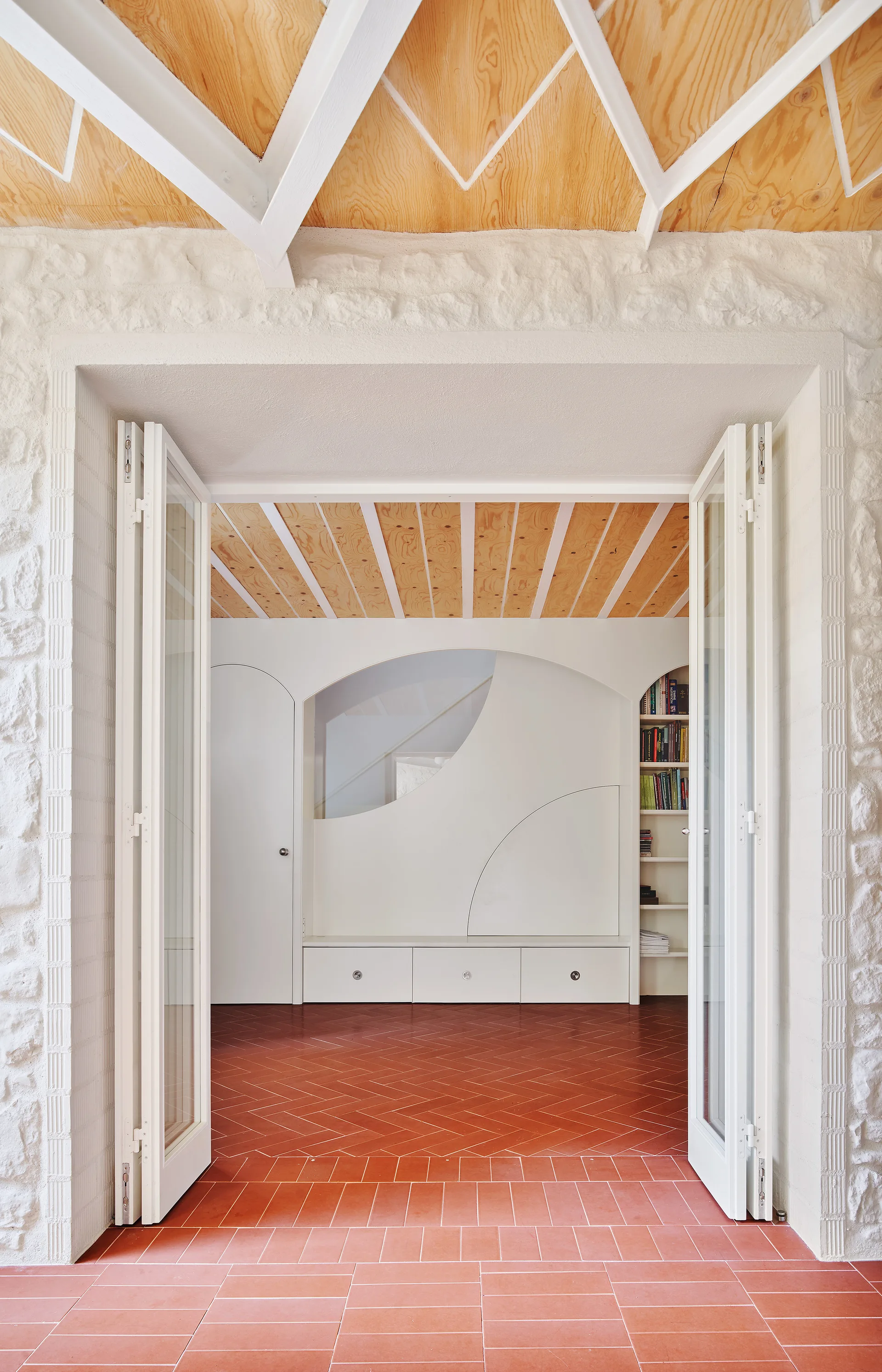 A view through open white folding doors into a hallway with red herringbone tile flooring and curved built-in cabinets.