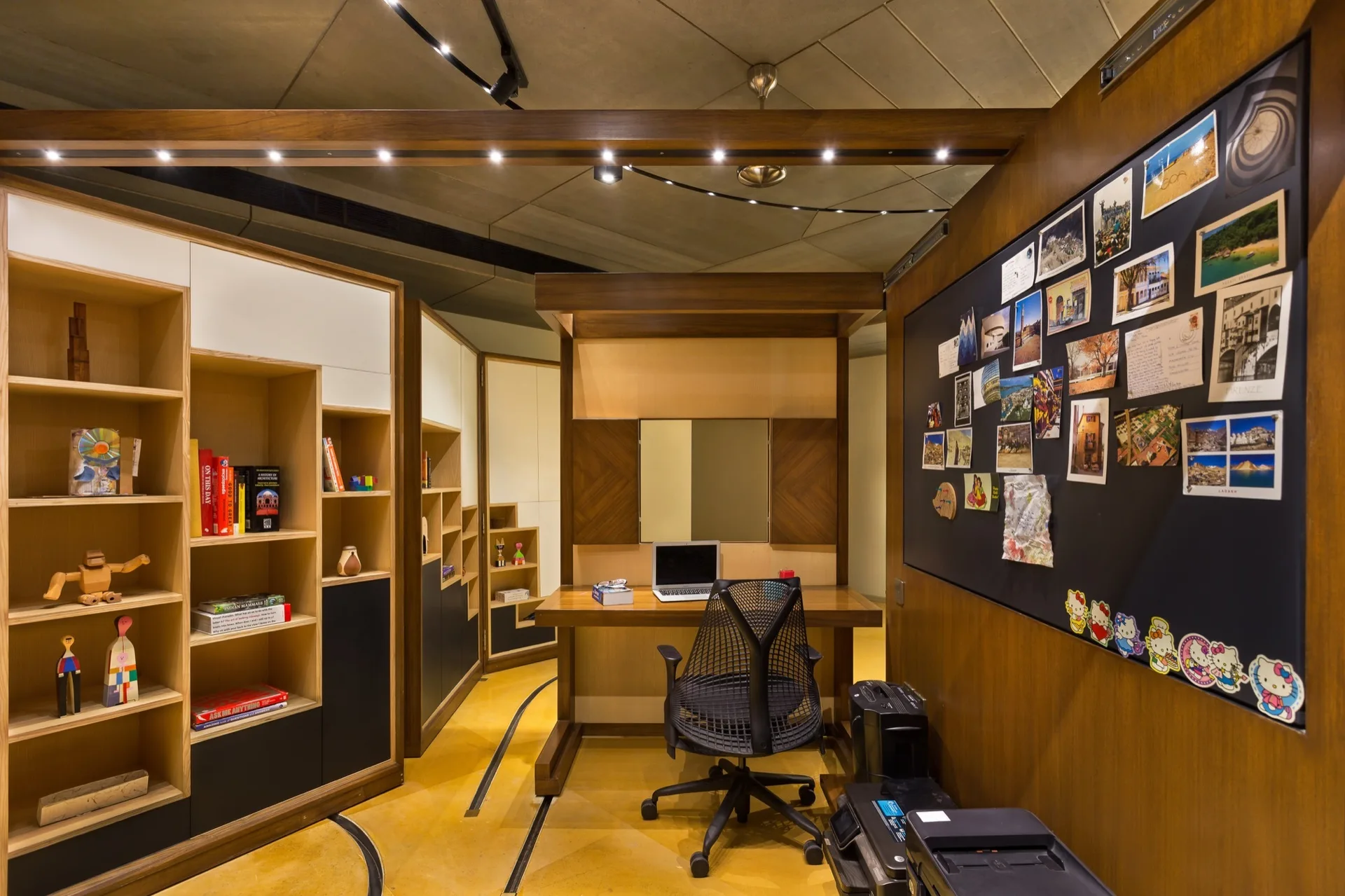 A contemporary home office features custom wood cabinets and shelving, an alcove desk with a black mesh chair, and a vibrant yellow floor.
