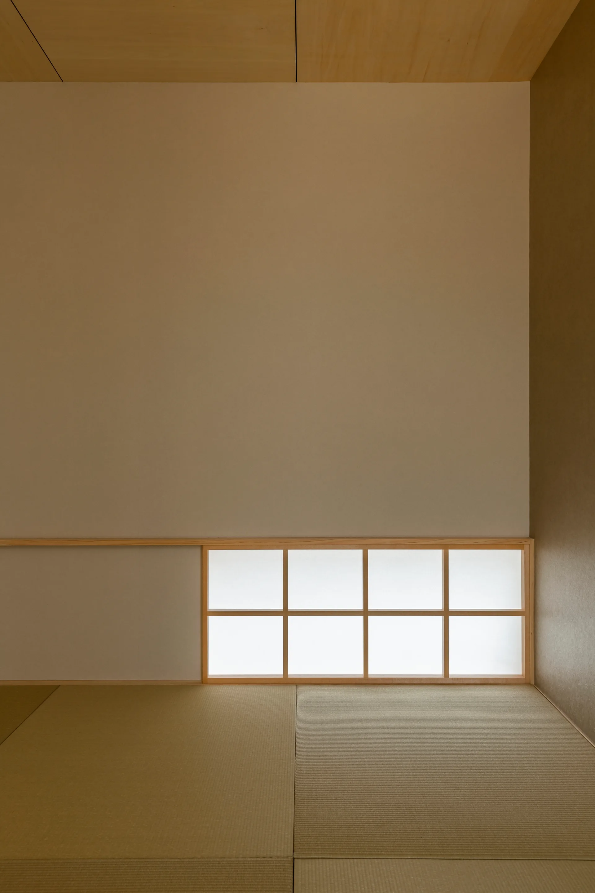 A minimalist Japanese room featuring textured tatami mat flooring, a low-profile wood grid shoji screen window, and smooth neutral walls.