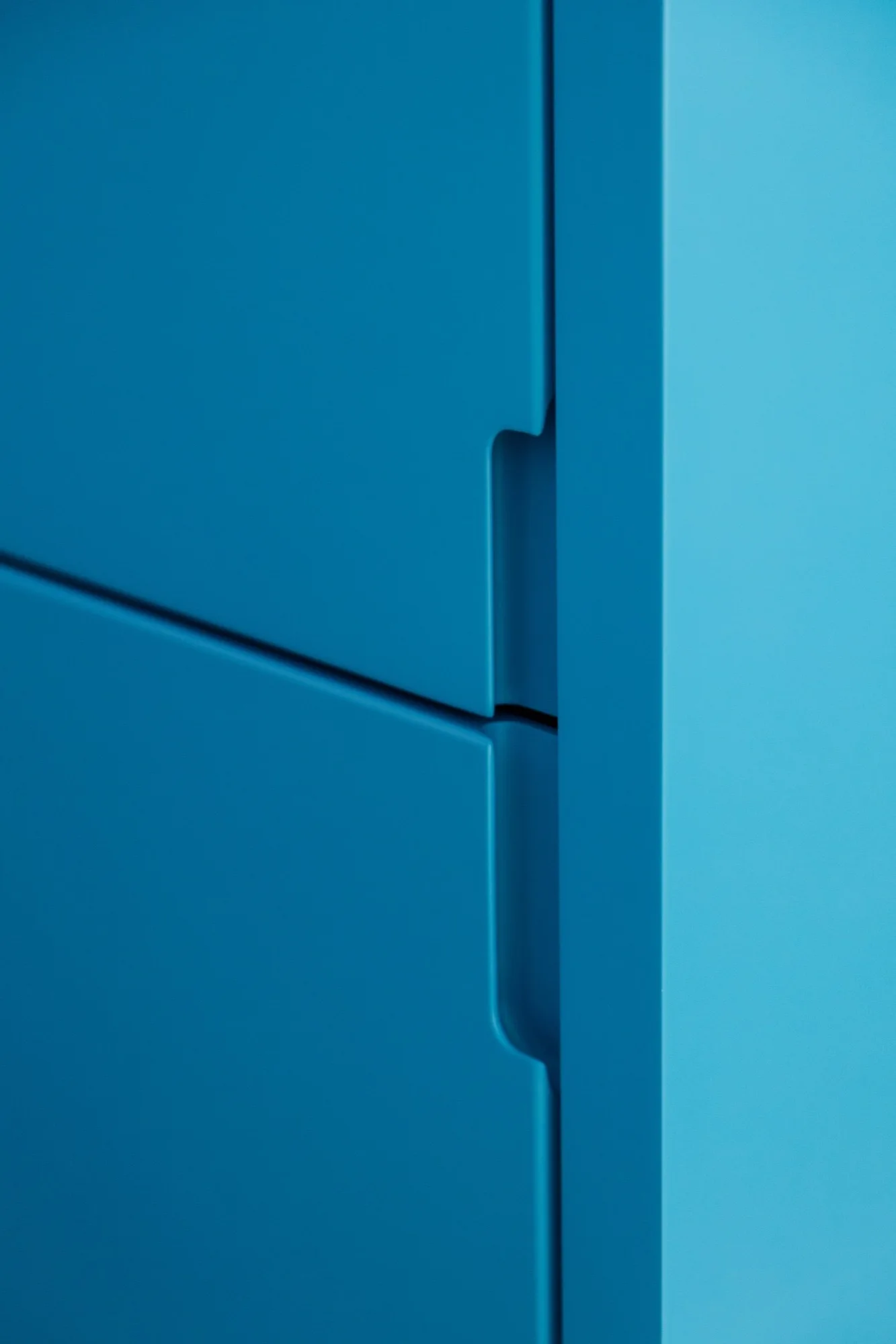 A close-up of matte blue cabinet doors featuring vertical recessed pull handles integrated into the flat panels.
