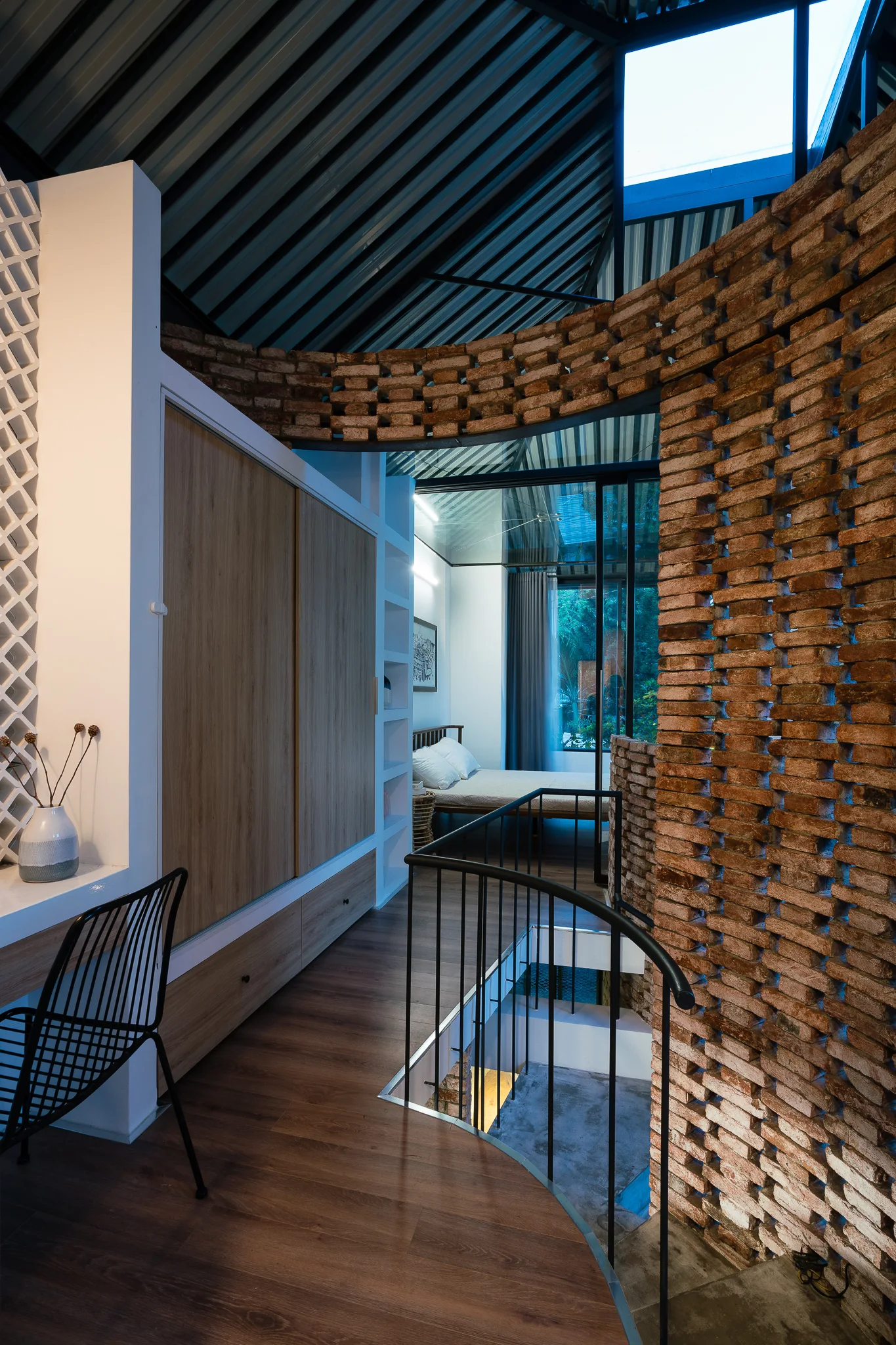 A modern bedroom loft features a curved terracotta brick screen wall next to a wood-planked staircase landing and built-in closet cabinetry.