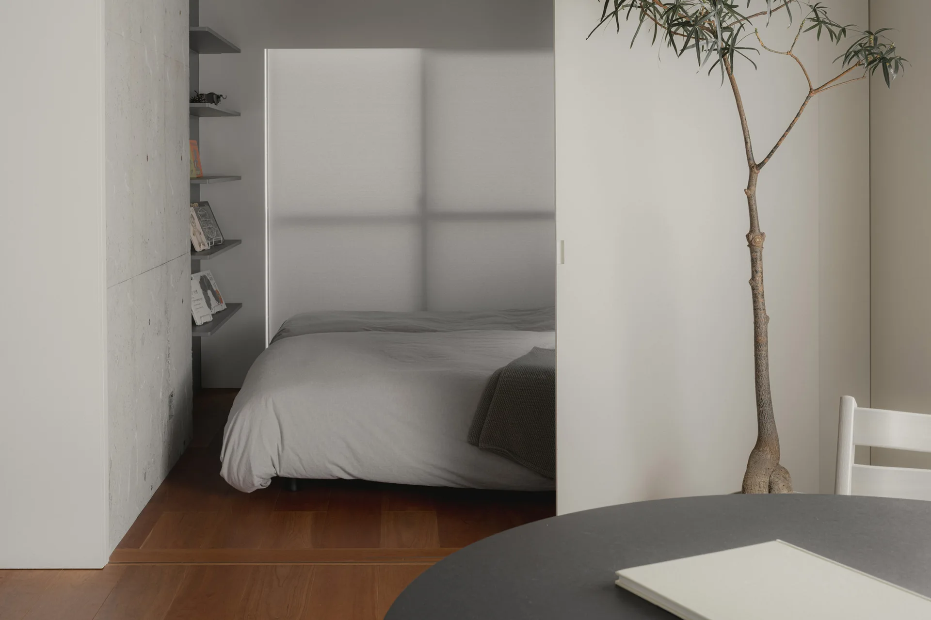 A minimalist bedroom is partially visible through an open white sliding door next to warm wood floors and a potted plant.