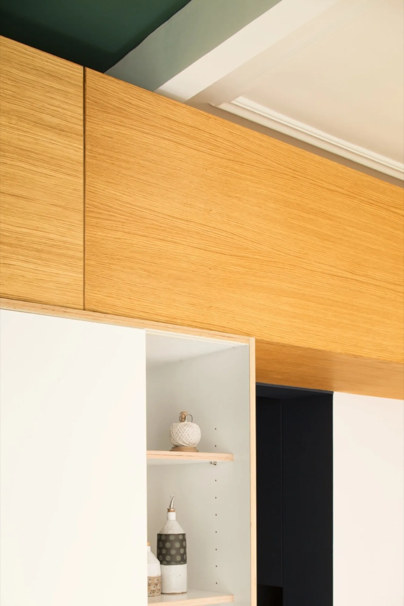 A close-up of custom cabinetry featuring natural wood grain upper panels, matte white doors, and an integrated open shelving niche displaying ceramic bottles.