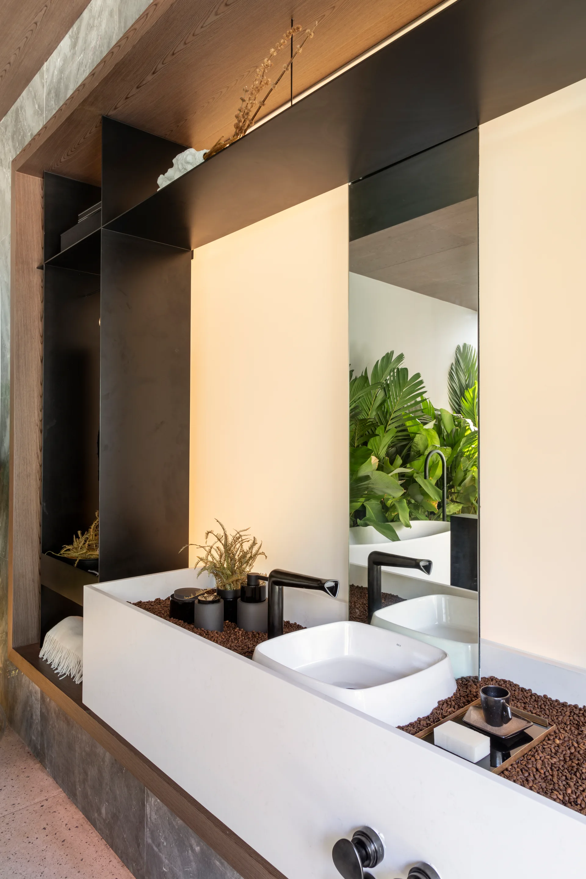 A modern bathroom vanity features a white square basin nestled within a tray of brown coffee beans beneath a tall vertical mirror.