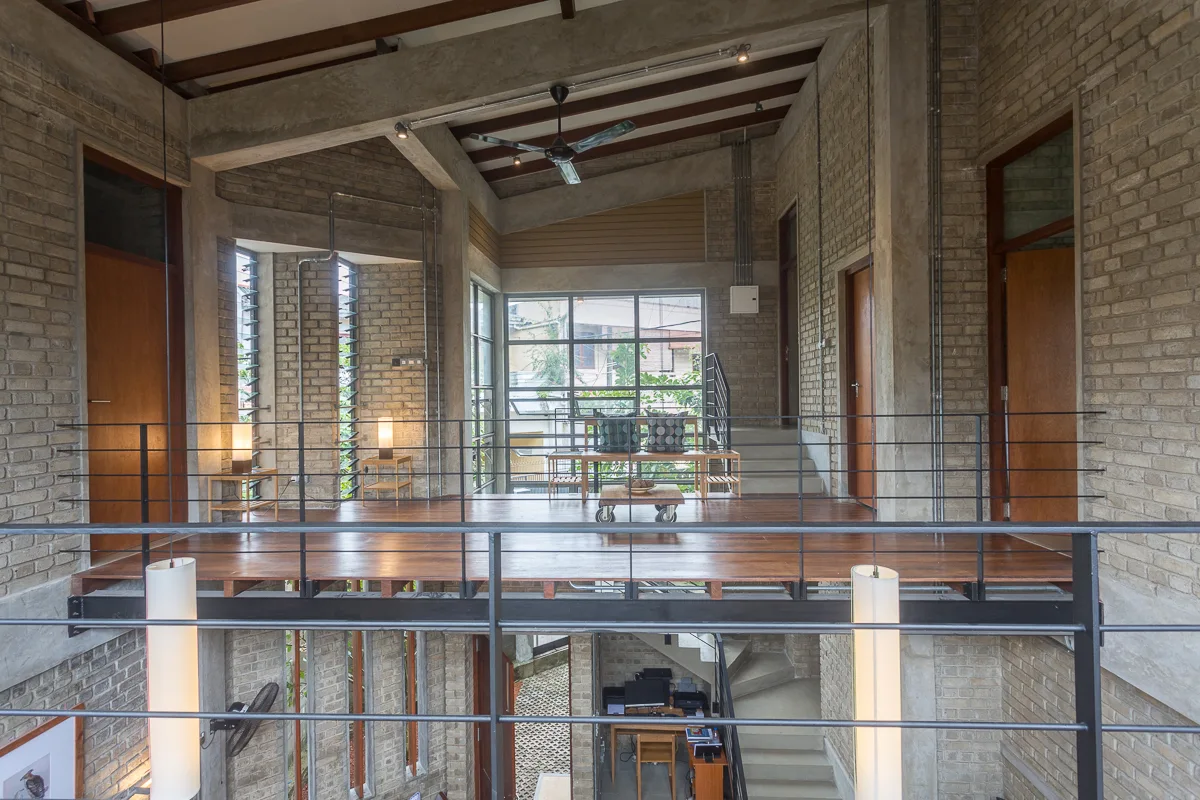 An elevated wooden mezzanine landing features light-colored exposed brick walls, a black metal railing, and a large multi-pane window.