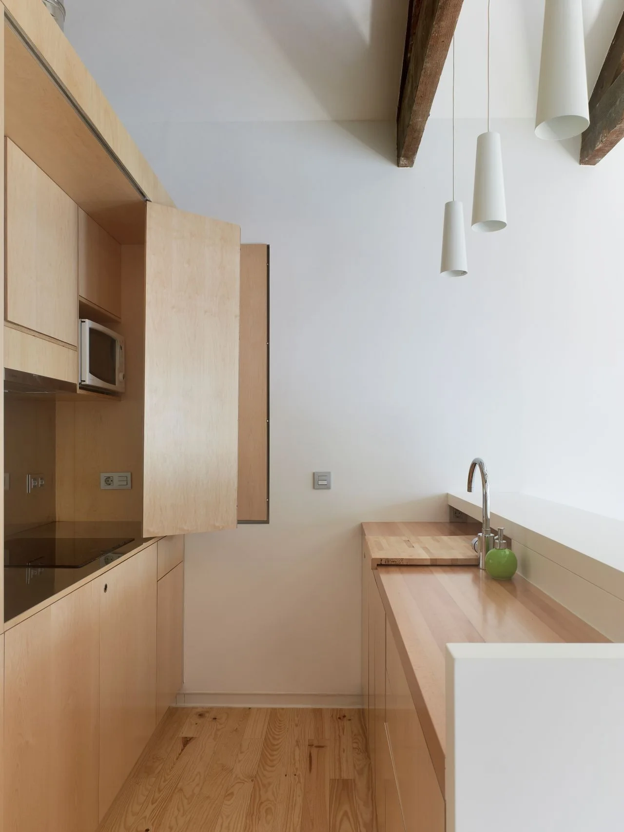 Minimalist galley kitchen featuring light wood cabinets, matching wood countertops, a chrome faucet, and three hanging white conical pendant lights.