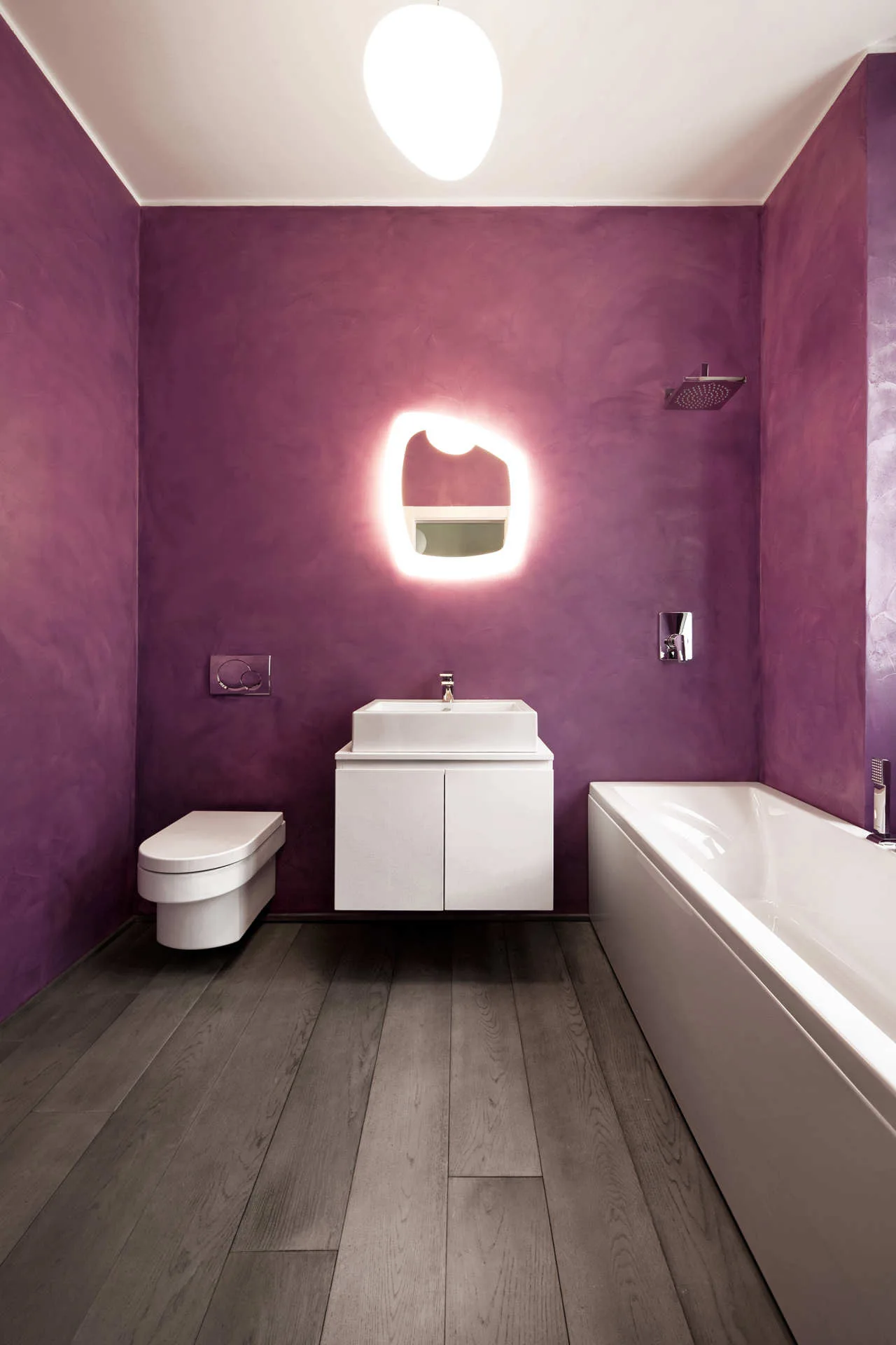 A modern bathroom features textured purple plaster walls, a wall-mounted white vanity with a backlit mirror, a floating toilet, and a bathtub.