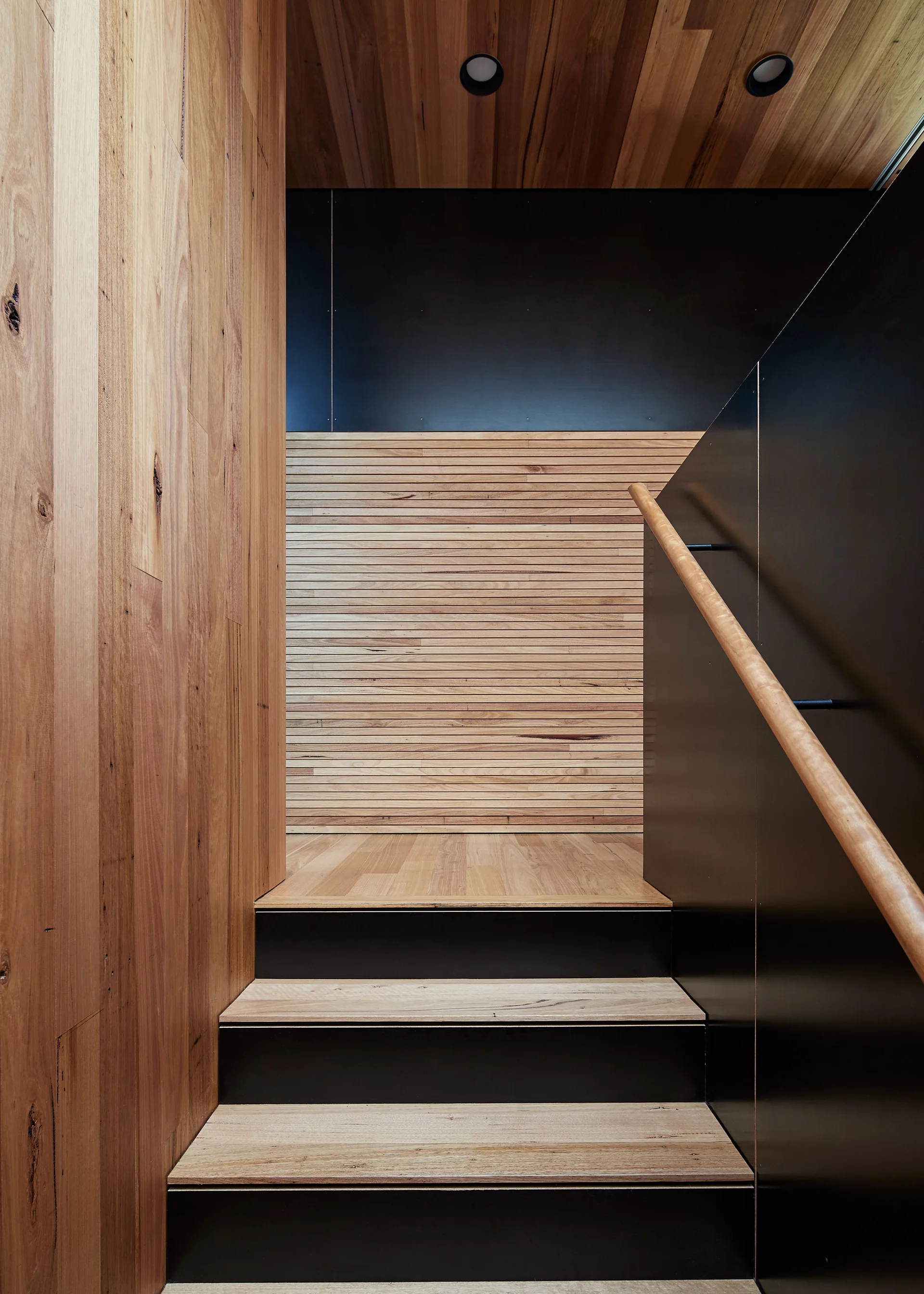 A modern minimalist staircase with wood treads and vertical plank wall cladding leading to a horizontal wood slat landing wall.