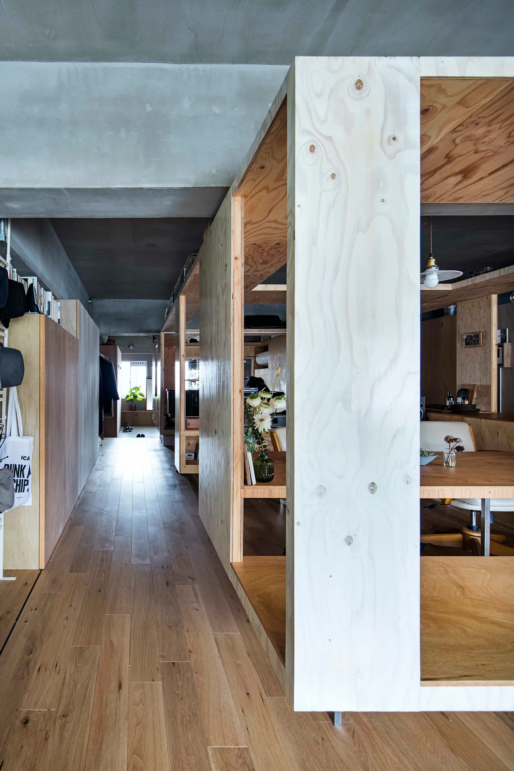 A modern open-plan interior featuring freestanding plywood partition structures, light hardwood floors, and a raw concrete ceiling.