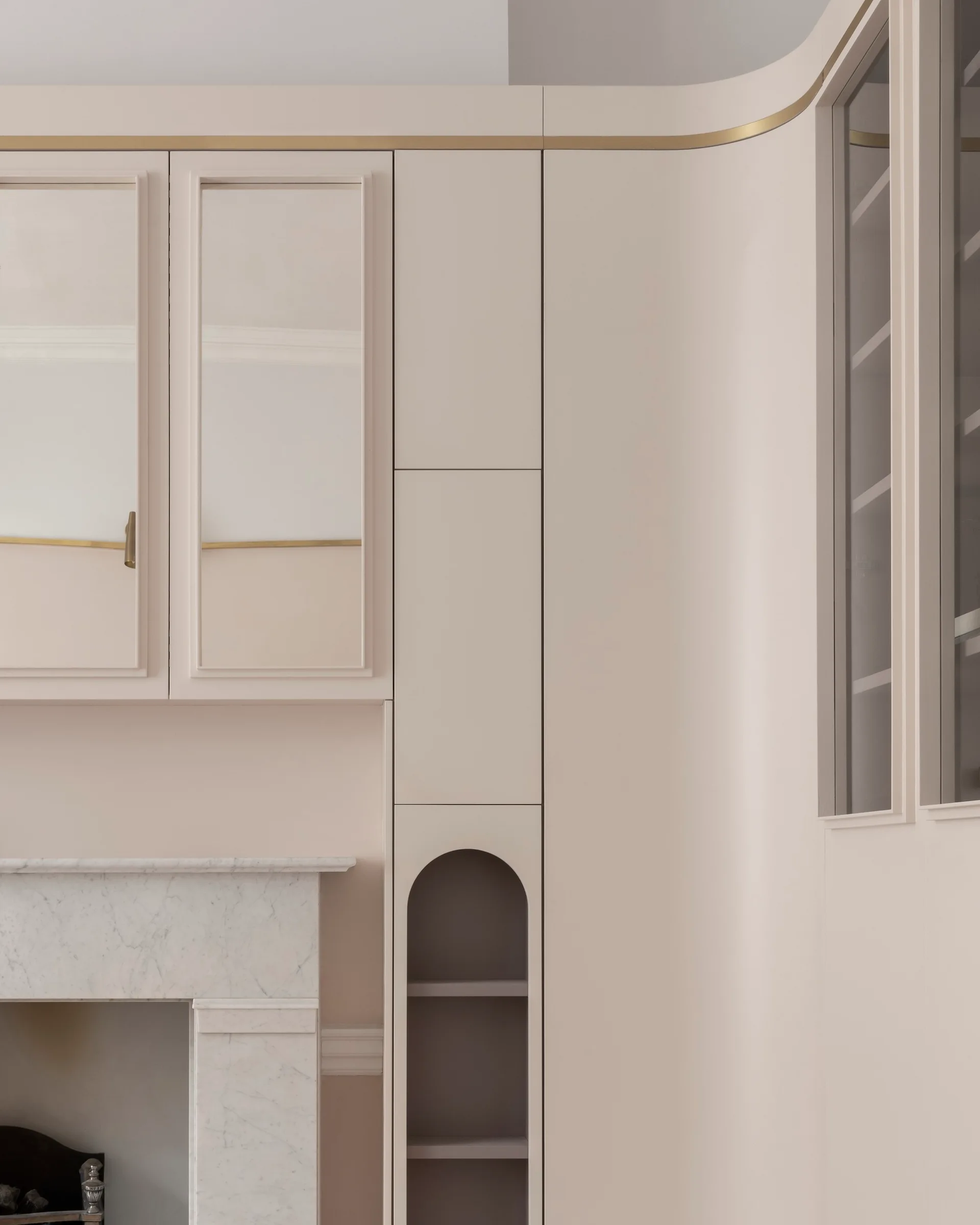 Bespoke pale pink living room cabinetry featuring a built-in arched display niche, glass doors, and a marble fireplace surround.