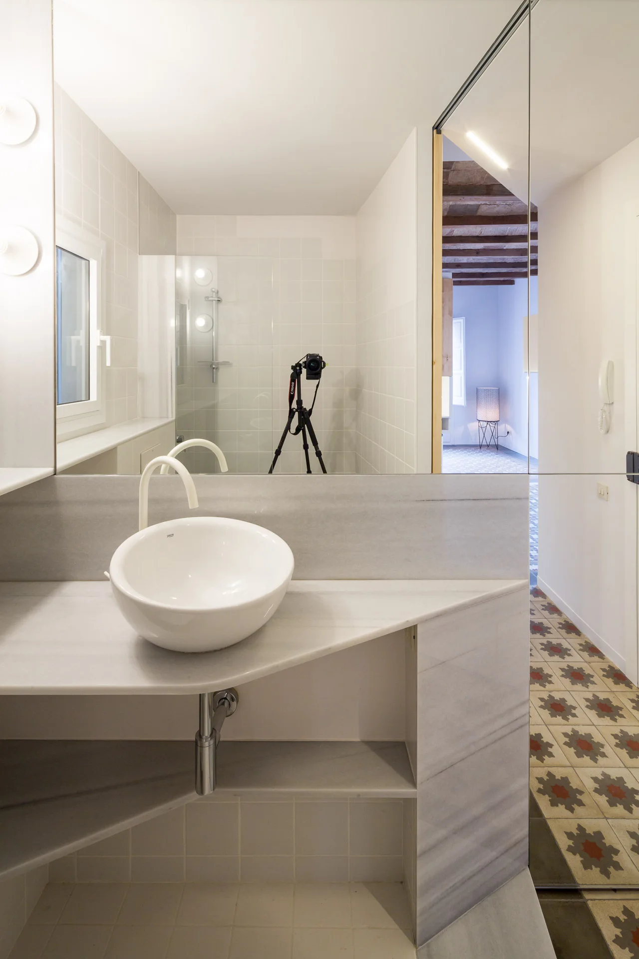 A minimalist bathroom featuring a grey stone vanity with a white vessel sink, a white faucet, and a large wall mirror.