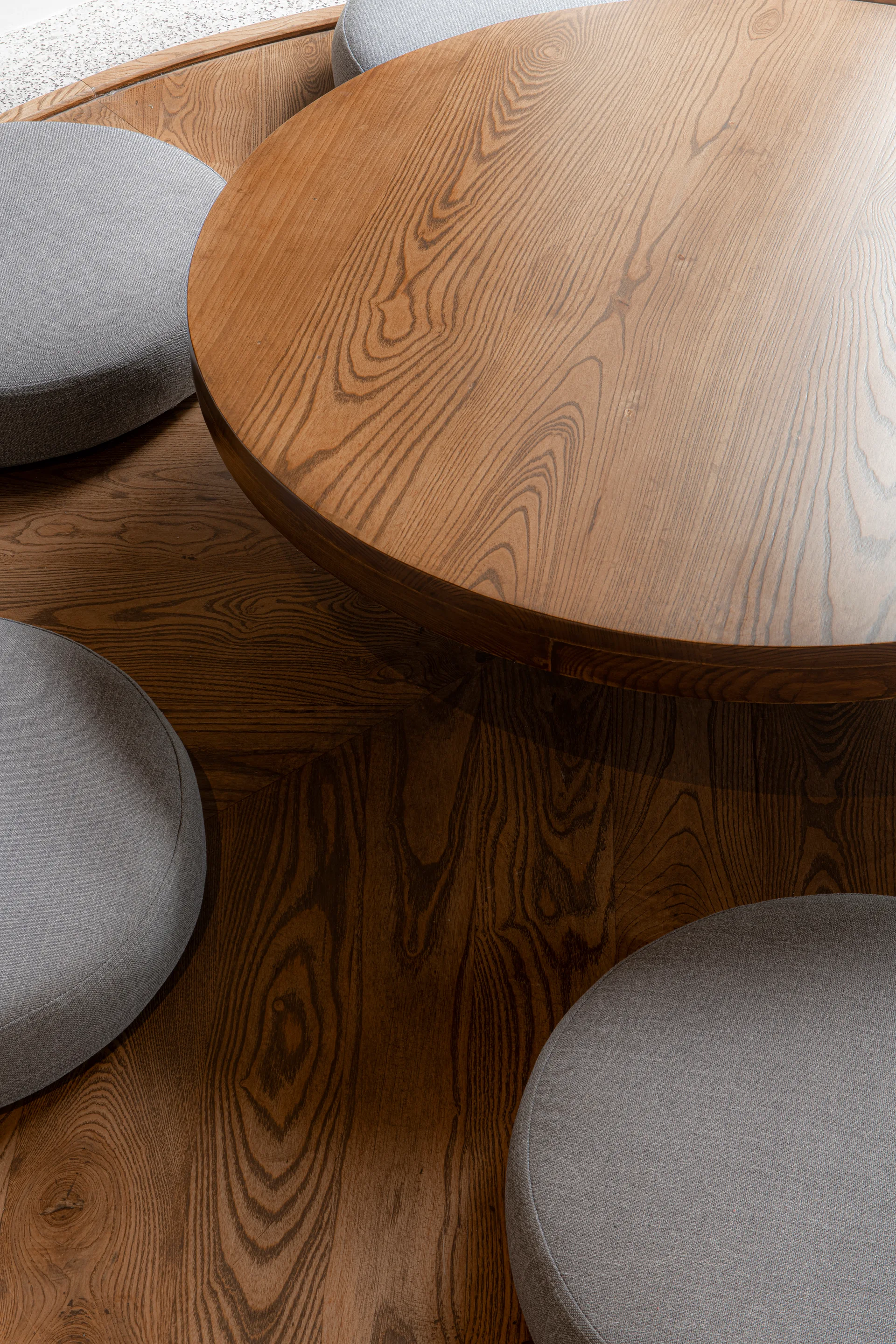 A high-angle close-up shows a round wooden table surrounded by circular grey fabric floor cushions on a wood grain floor.
