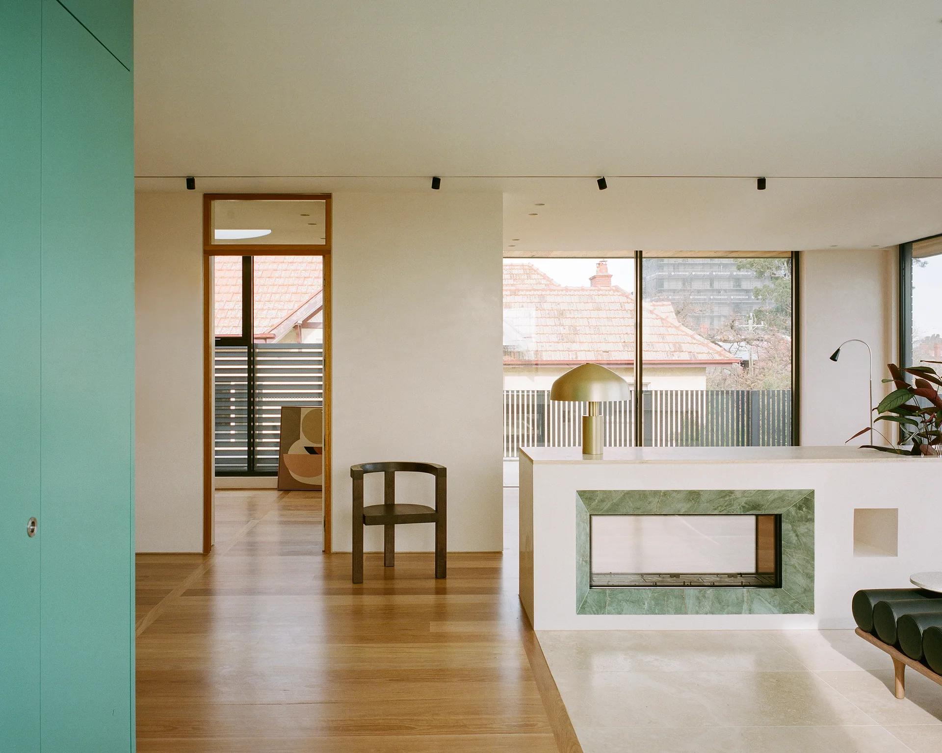 A minimalist living room with a low white fireplace divider featuring green stone, wood floors, a brass dome lamp, and a teal built-in cabinet.