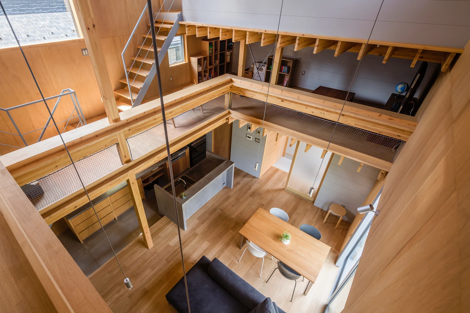 High-angle view of an open-concept living space with light wood paneling, a mezzanine loft with a mesh safety net, and a concrete kitchen island.